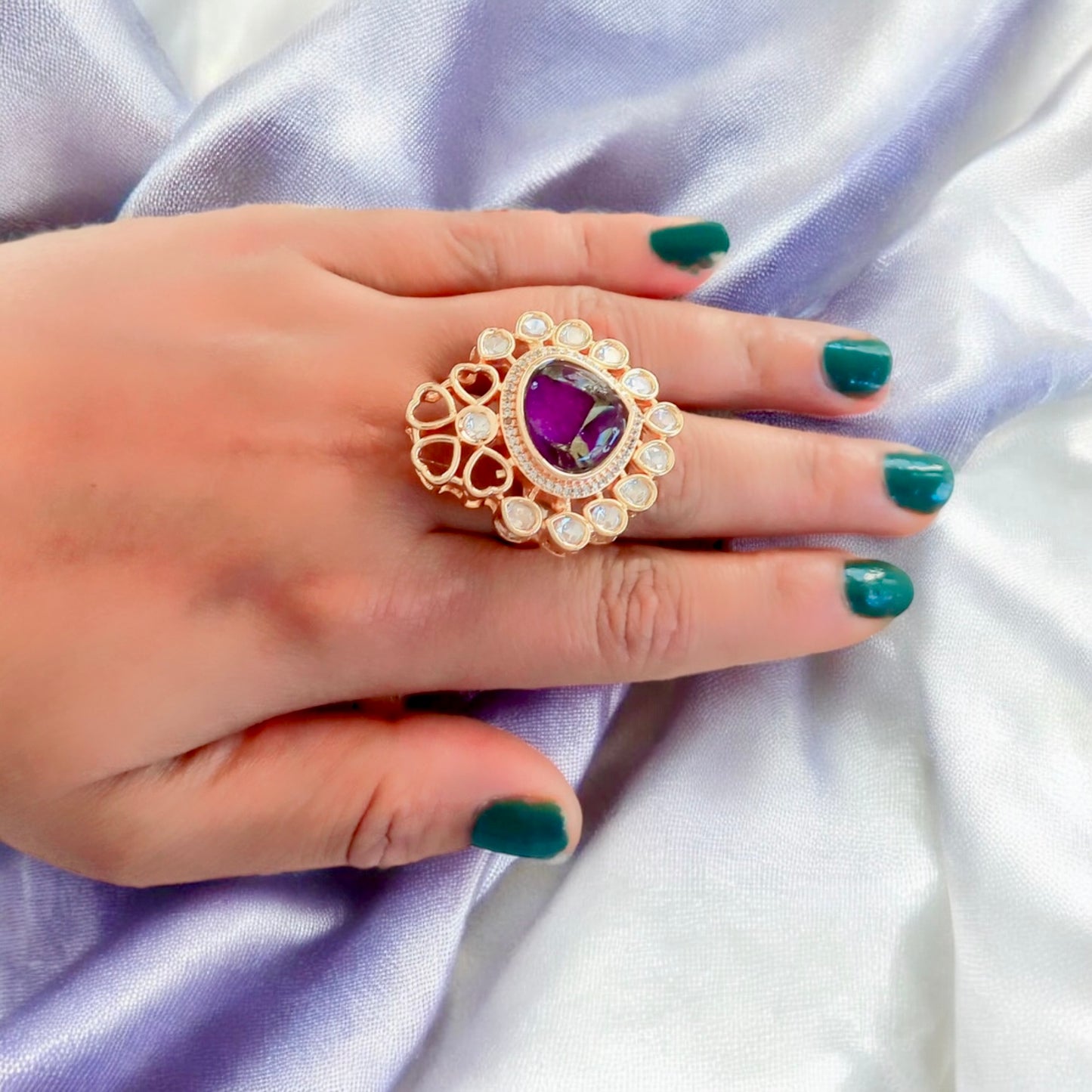 Elegant adjustable Polki Kundan finger ring with a bold purple center stone surrounded by intricate gold and diamond accents worn on a hand with green nail polish.