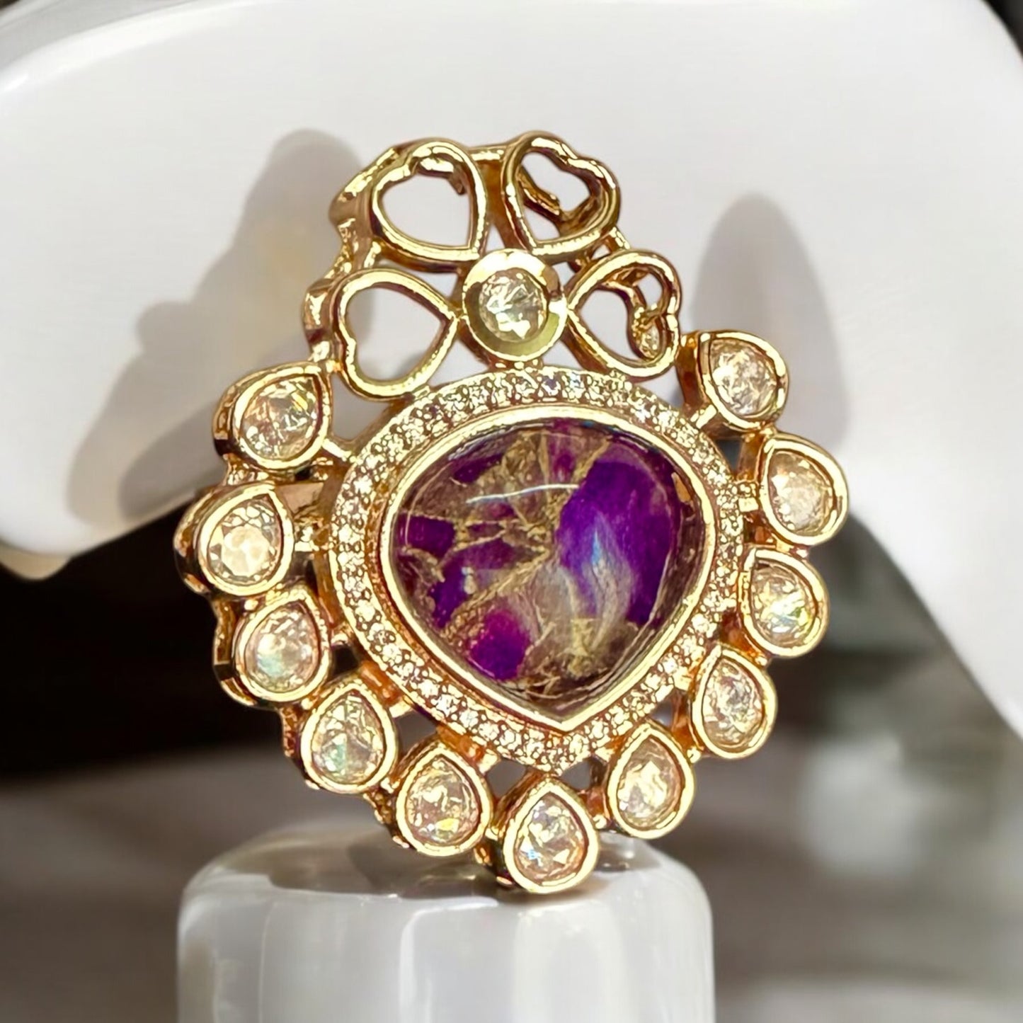 Elegant adjustable Polki Kundan finger ring with a bold purple center stone surrounded by intricate gold and diamond accents. It is showcased on a white jewellery display stand.