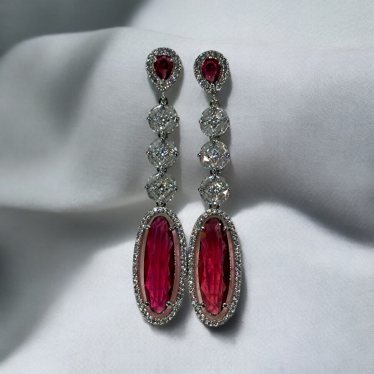 Ruby Colored American Diamond Statement Earrings on a dull white fabric background