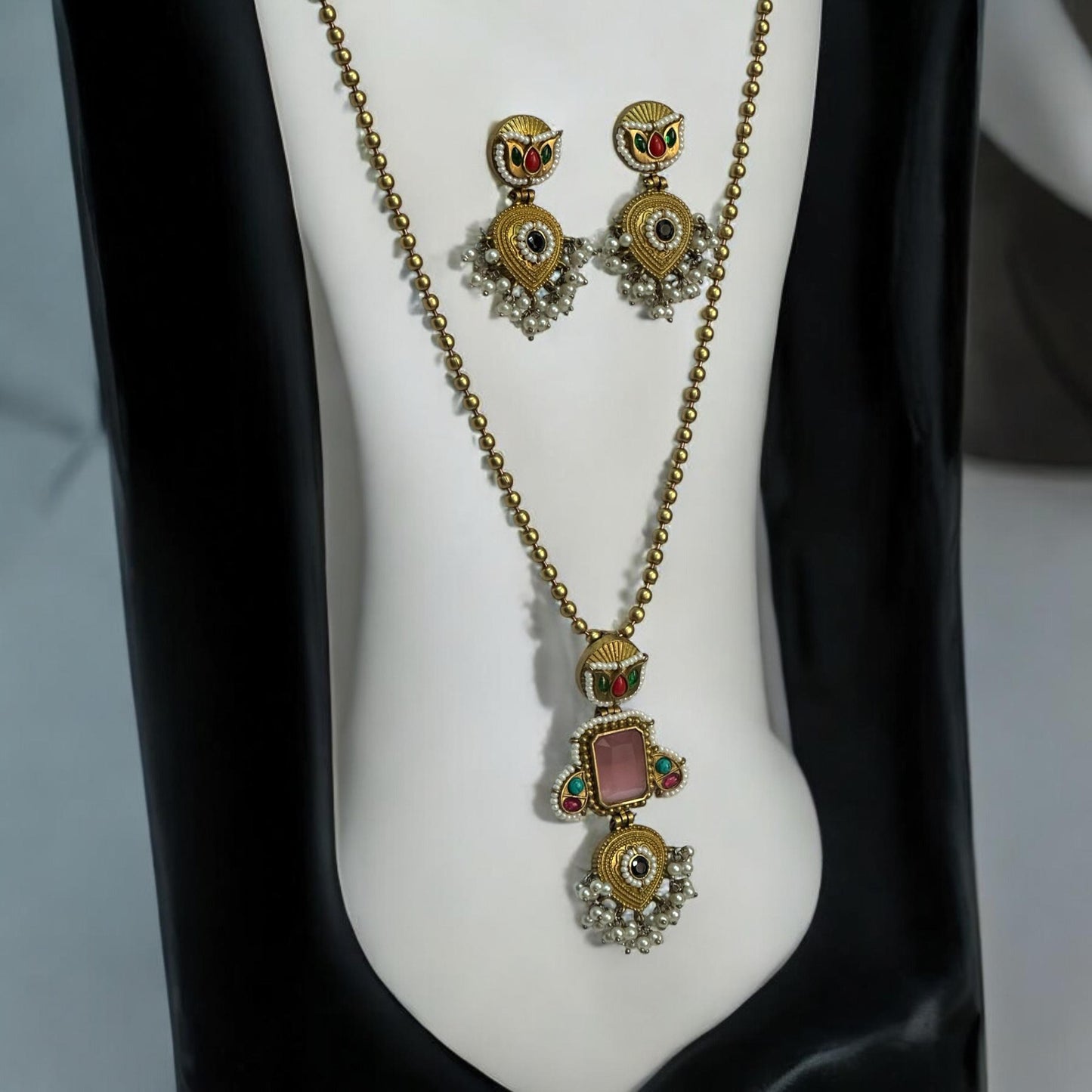 Amrapali Pachi Kundan Long Chain Pendant Set with Pink Monalisa Stone, featuring intricate detailing and matching earrings on a white and black jewellery display stand.