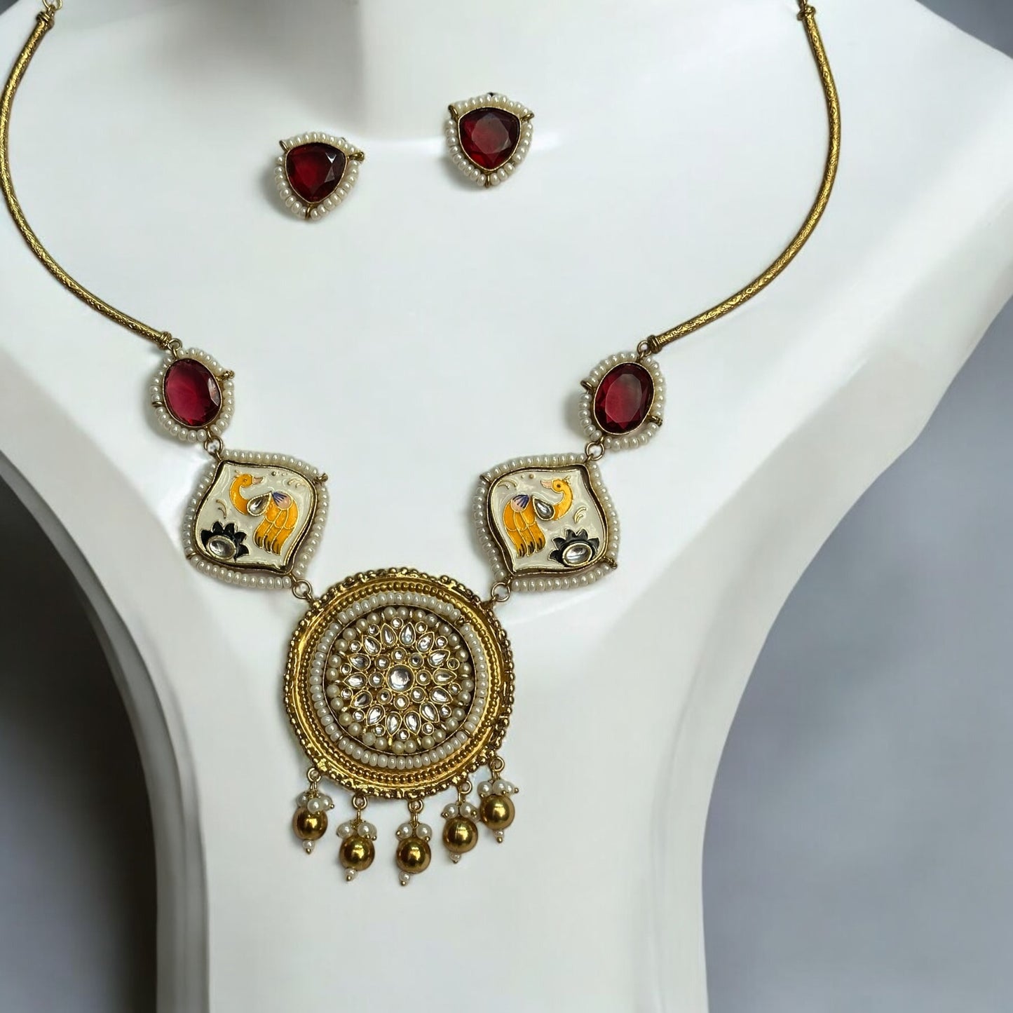 Amrapali Designer Hand-Painted Red Necklace with Studs – a traditional masterpiece with pearl detailing, Kundan stones, and intricate hand-painted motifs. It is placed on a white jewellery display stand in the image.