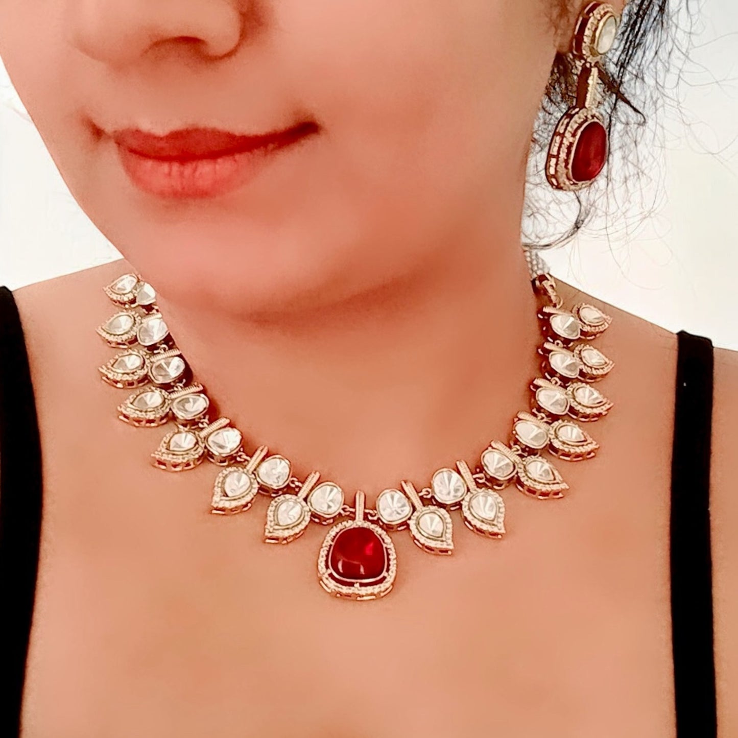 A model displaying a Elegant designer polki kundan necklace with teardrop accents and red gemstone centerpiece, paired with matching earrings.