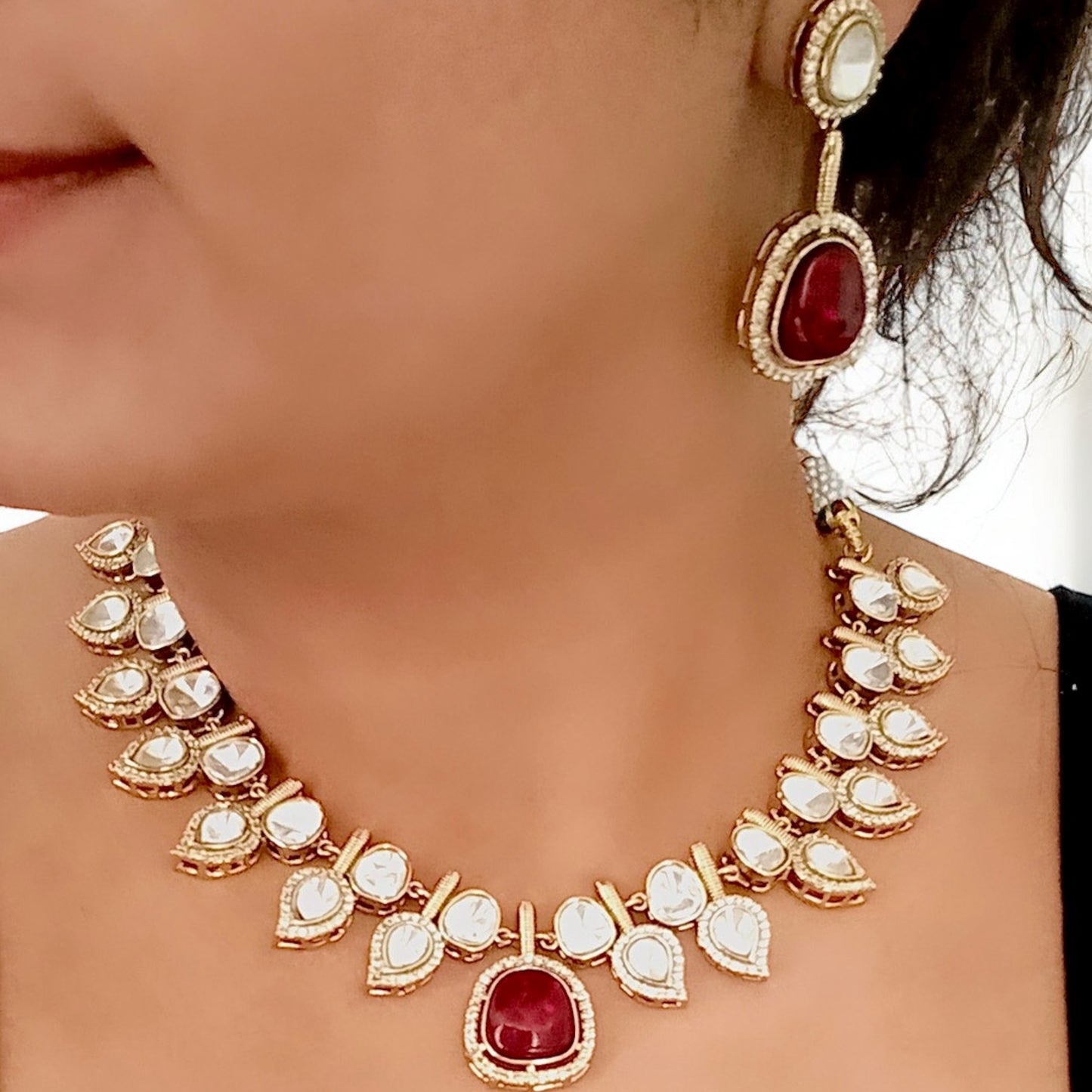 A model wearing and Displaying a Elegant designer polki kundan necklace with teardrop accents and red gemstone centerpiece, paired with matching earrings.