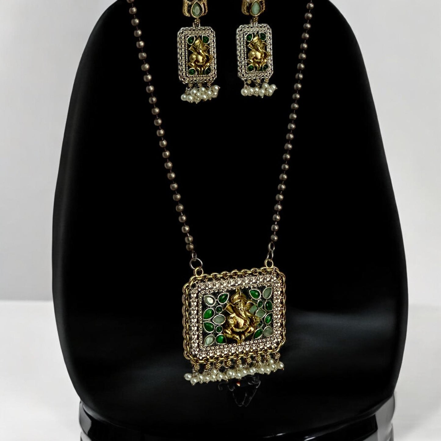 Dual-tone silver replica long chain pendant set featuring a god figure in gold-tone, adorned with green and white accents, displayed on a black mannequin against a plain white background.