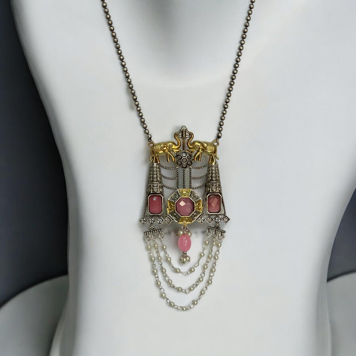 Dual-tone Silver Replica Long Pendant Necklace with Pink Monalisa Stone Accents and Intricate Chain Detailing PLACED ON A WHITE COLOURED JEWELLERY DISPLAY STAND.