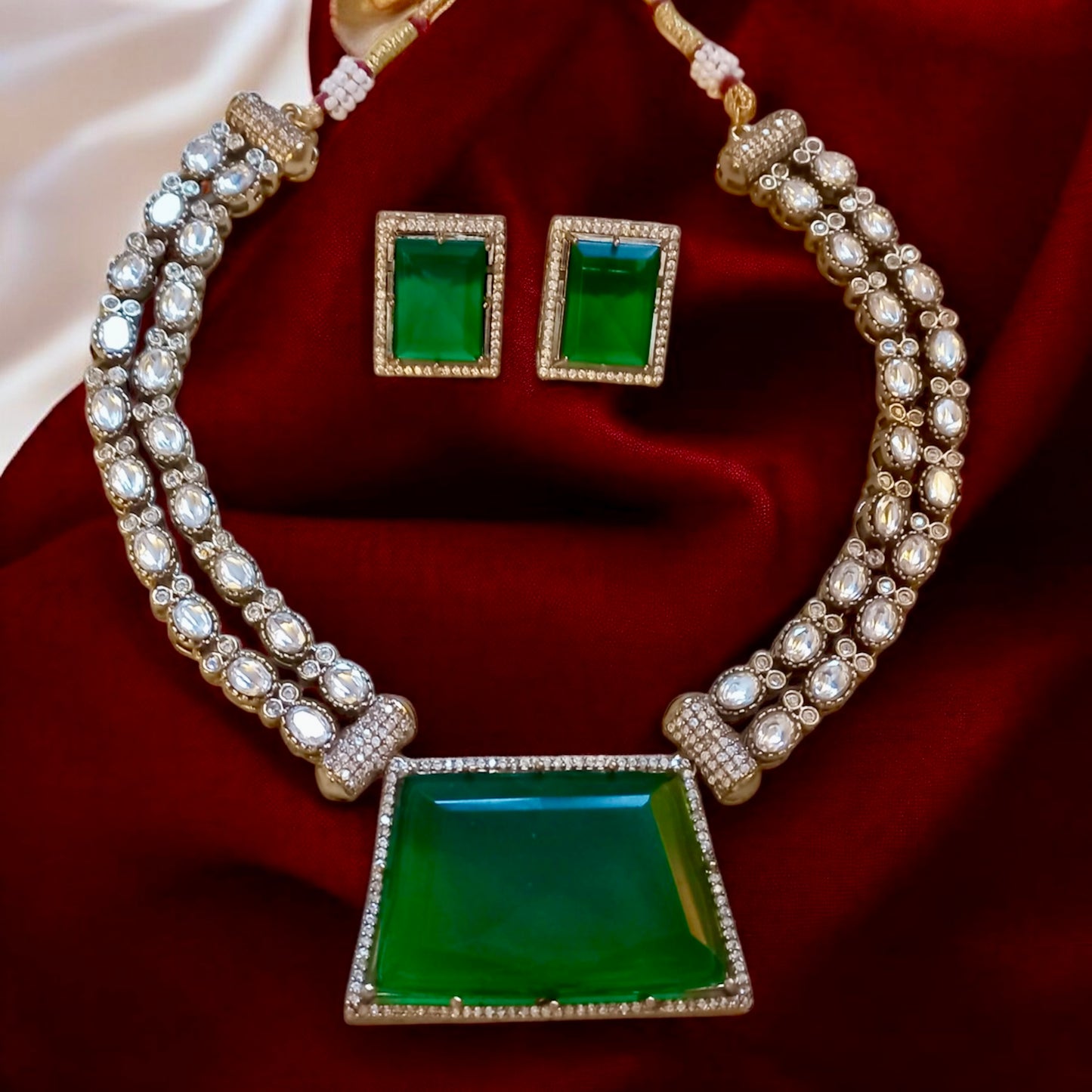 Emerald green moissanite double layer necklace set with crystal-studded pendant and matching rectangular earrings on Red velvet Fabric background