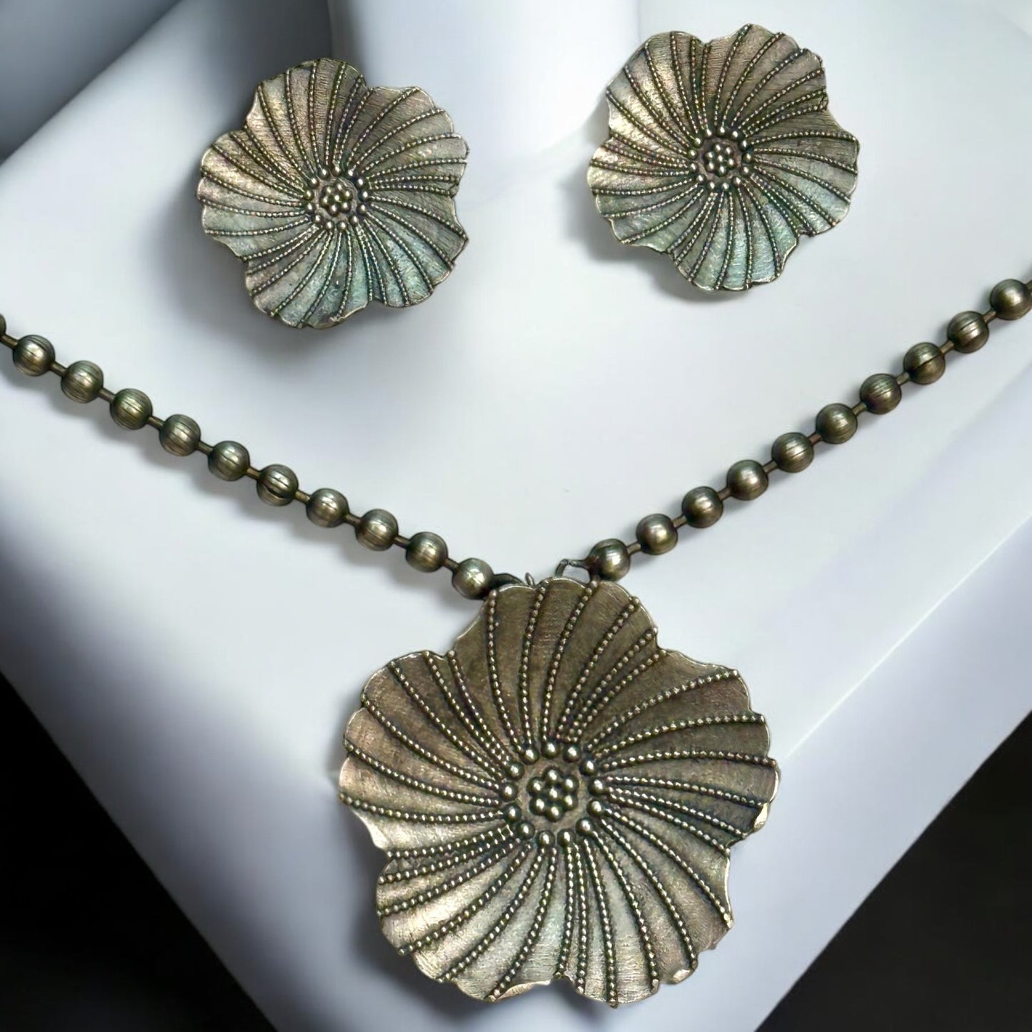 German silver chain pendant set featuring a large floral design pendant with intricate dotted detailing, paired with matching floral earrings. Displayed against a white background on a white color jewellery display stand.