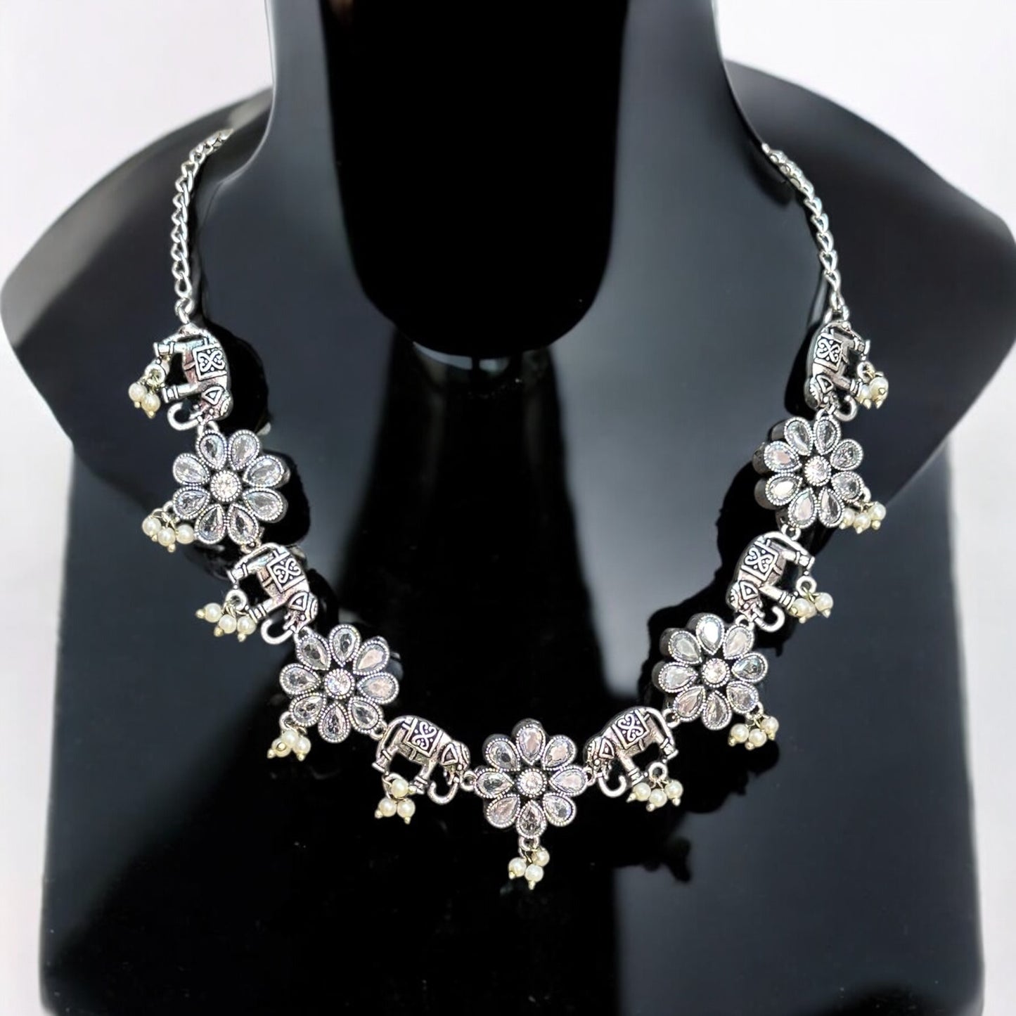 German silver necklace featuring intricate elephant motifs and floral pendants adorned with dangling pearls. Displayed on a black mannequin bust against a plain background.