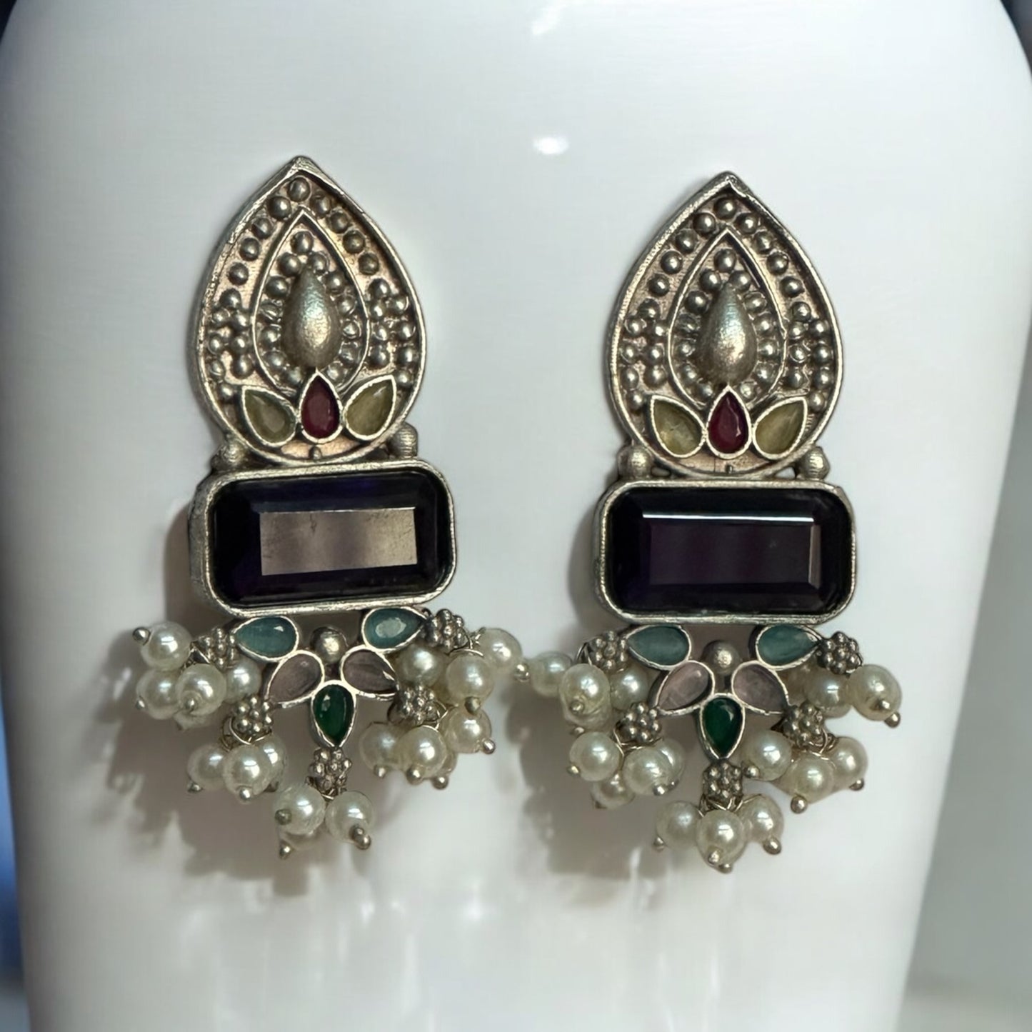 Ethnic German silver earrings with black stone centerpiece, multi-colored enamel detailing, and pearl accents on a white jewellery display stand.