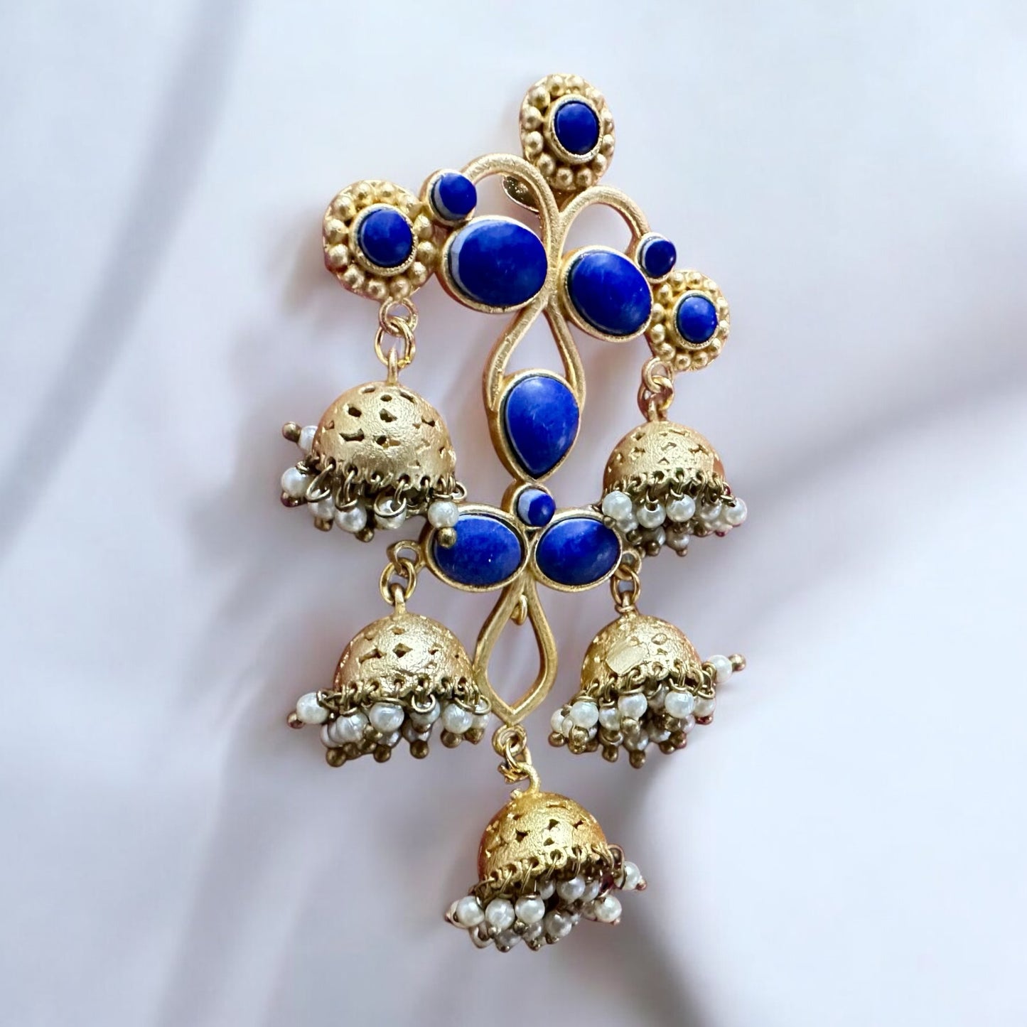 A single Gold Plated Statement Earring with dark blue stones on a white fabric background.
