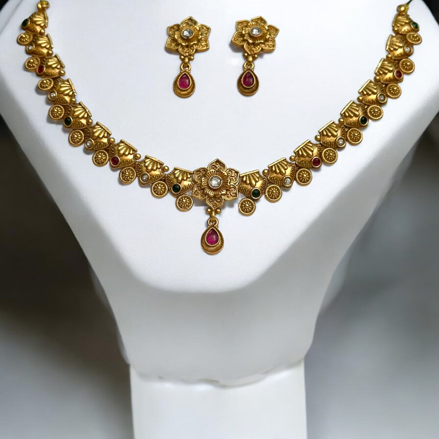Golden Rajwadi Minimal Necklace Set featuring an intricately detailed necklace adorned with tiny floral and gemstone accents, paired with matching earrings. Displayed on a white jewellery display stand against a soft background.