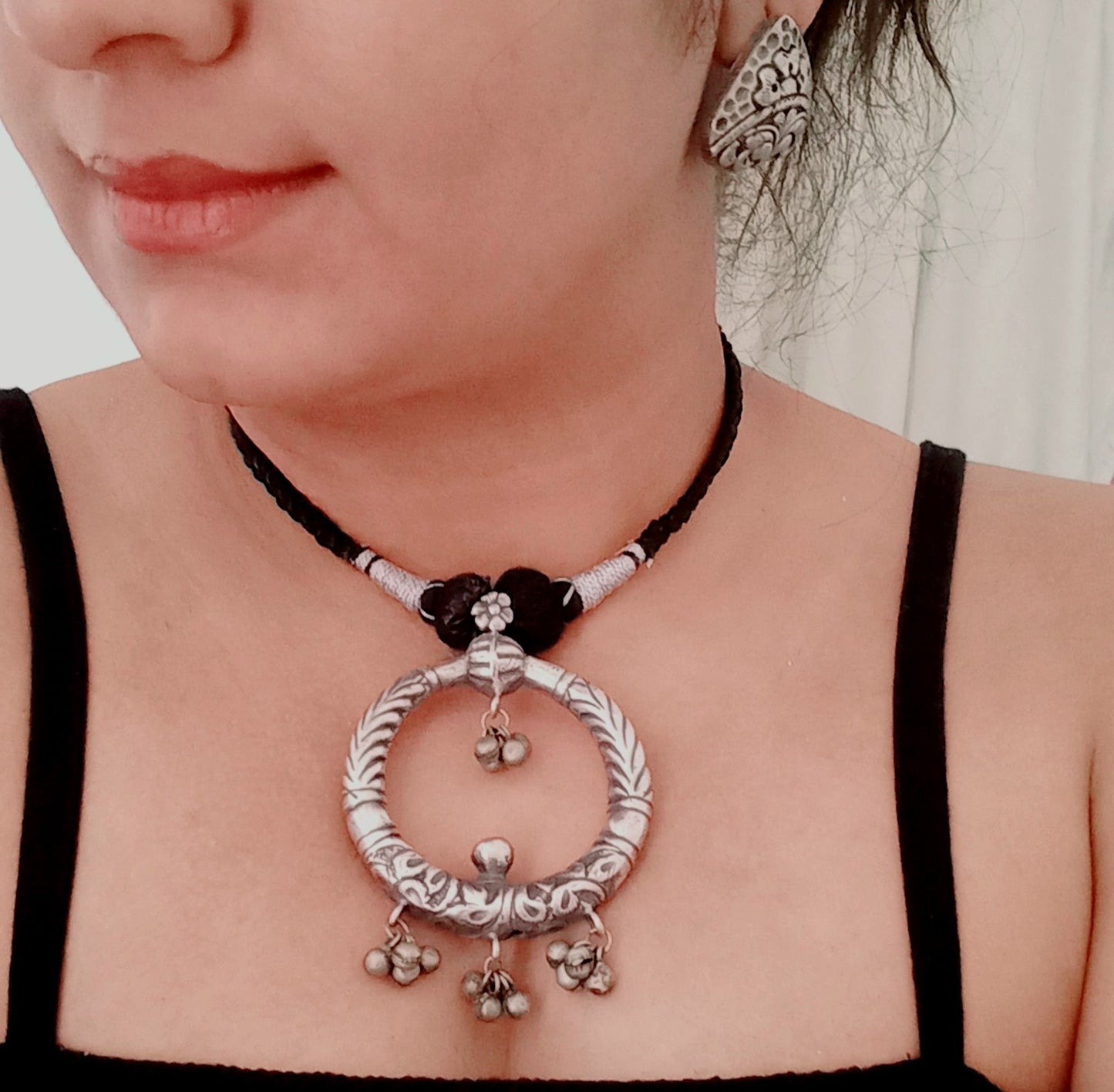 A model displaying Handmade silver replica necklace featuring a bold circular pendant with intricate engravings and ghungroo charms, paired with detailed triangular stud earrings.