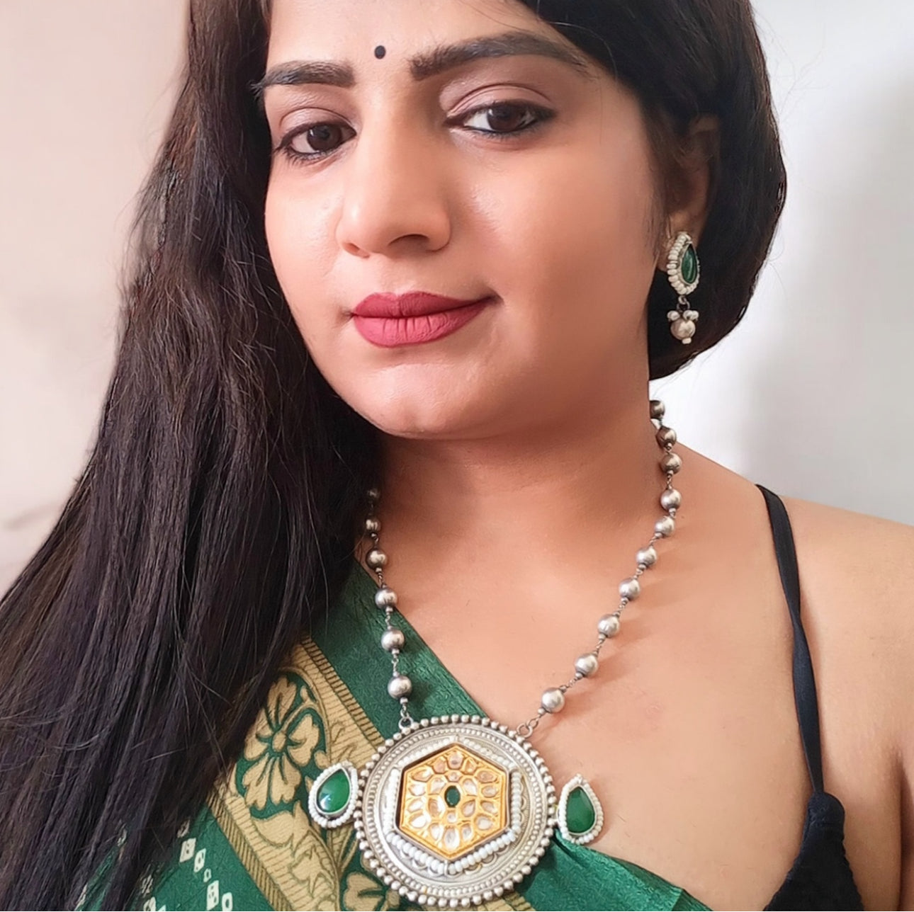 Model displaying a Long Dual Tone Apala Big Size Pendant Set in Green featuring an intricately designed silver-gold pendant with Kundan work, green stone accents, and matching teardrop earrings. Perfect for ethnic and festive wear.