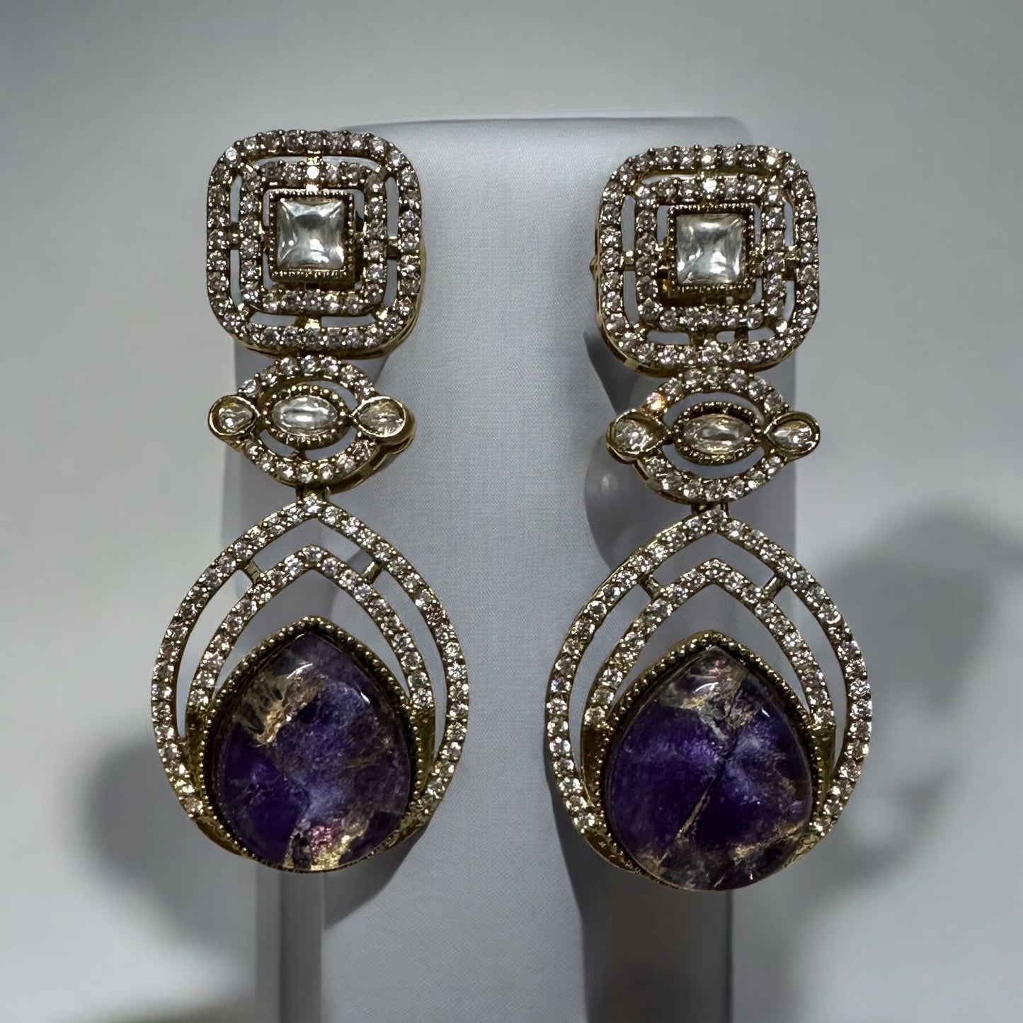 Moissanite Kundan With Doublet Amethyst purple Stone necklace set earrings placed on a grey colored jewellery display stand. Earrings also have small american diamonds on it.