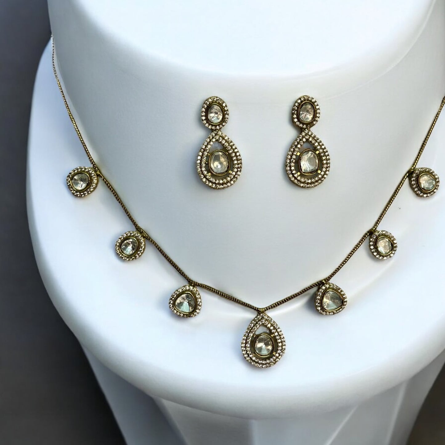 Moissanite chain design necklace set with earrings in golden colour places on a white colored jewellery display stand.