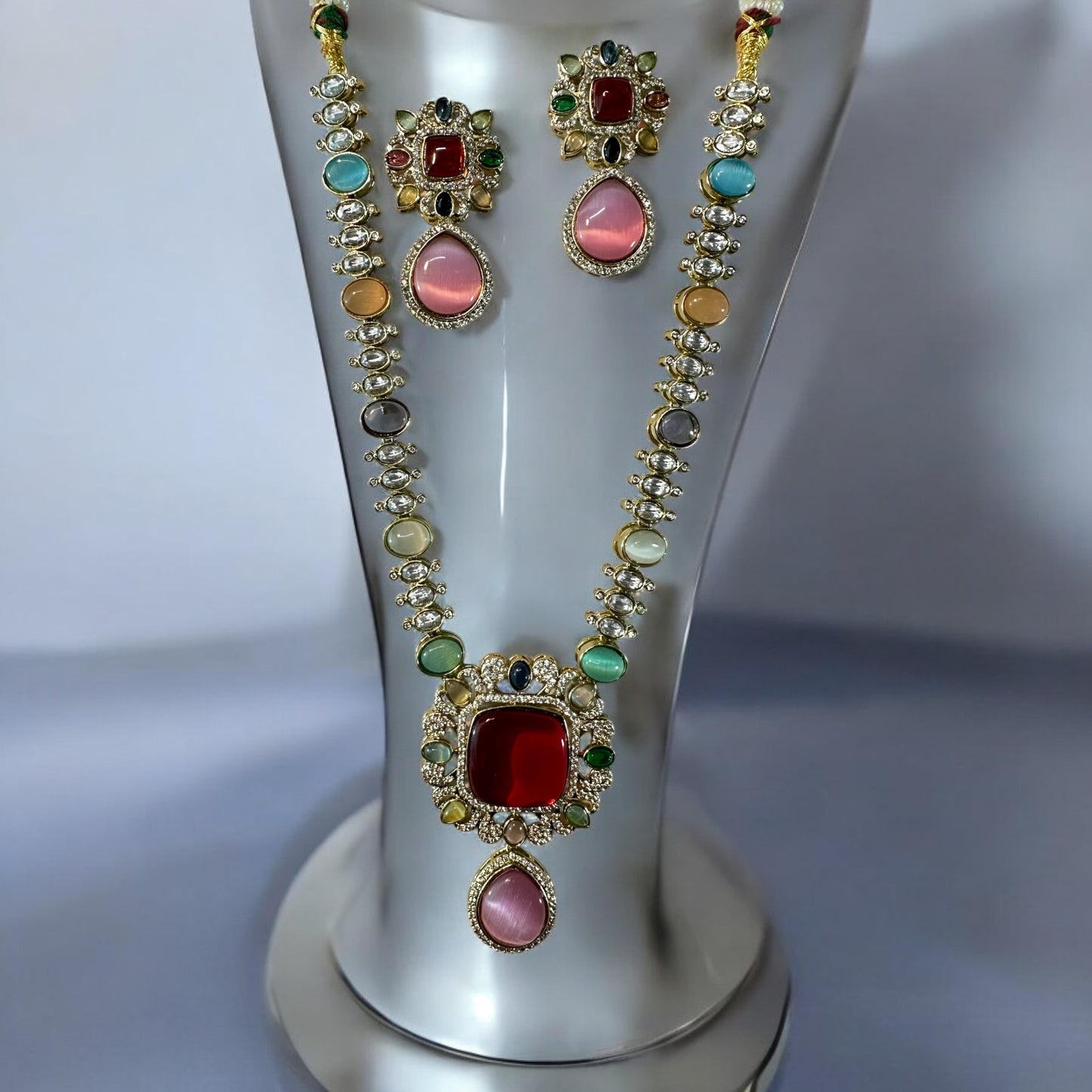 Moissanite Premium Multicolor Kundan Necklace and earrings with a centred red stone and multi colored stones on necklace's string with shiny crystals. It is placed on grey jewellery display stand.