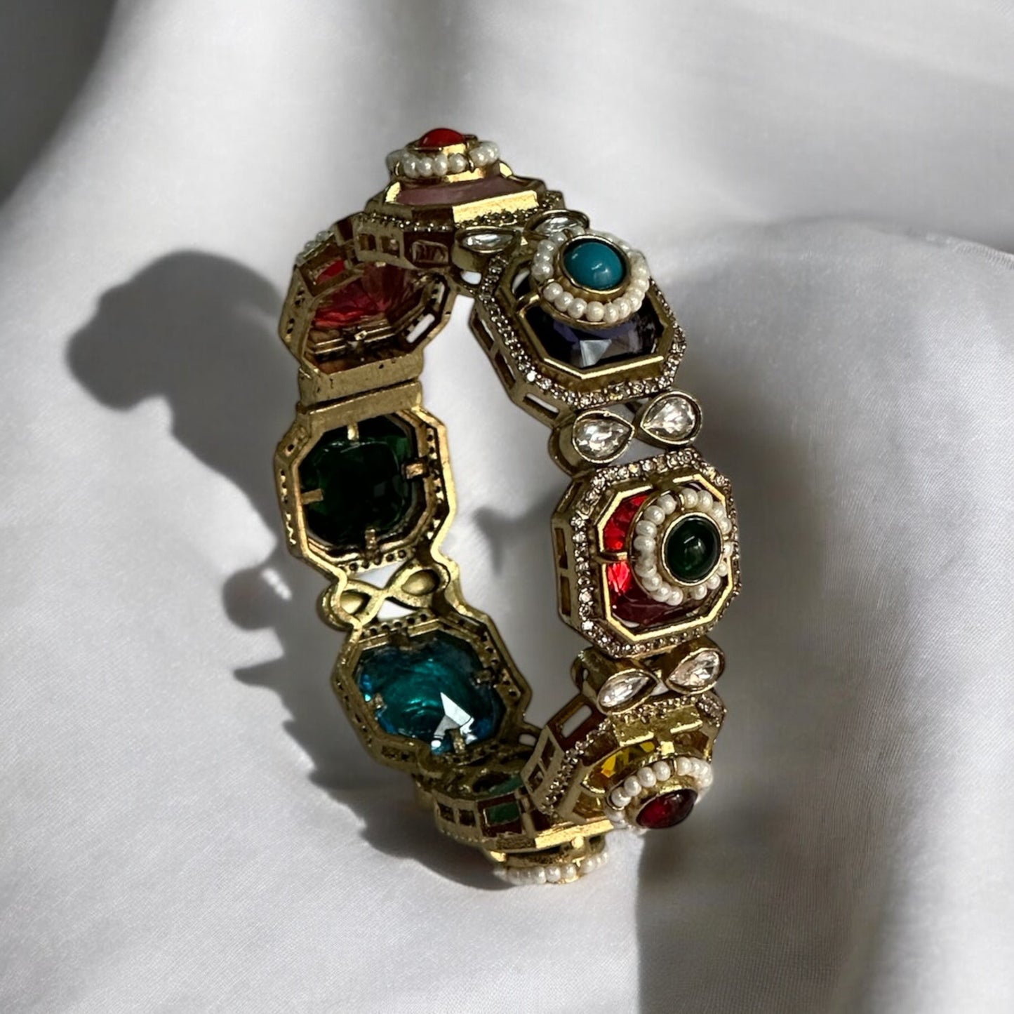 Exquisite single Pachi Kundan bangle adorned with colorful moissanite stones and delicate pearl detailing. Kada is standing on a white fabric.