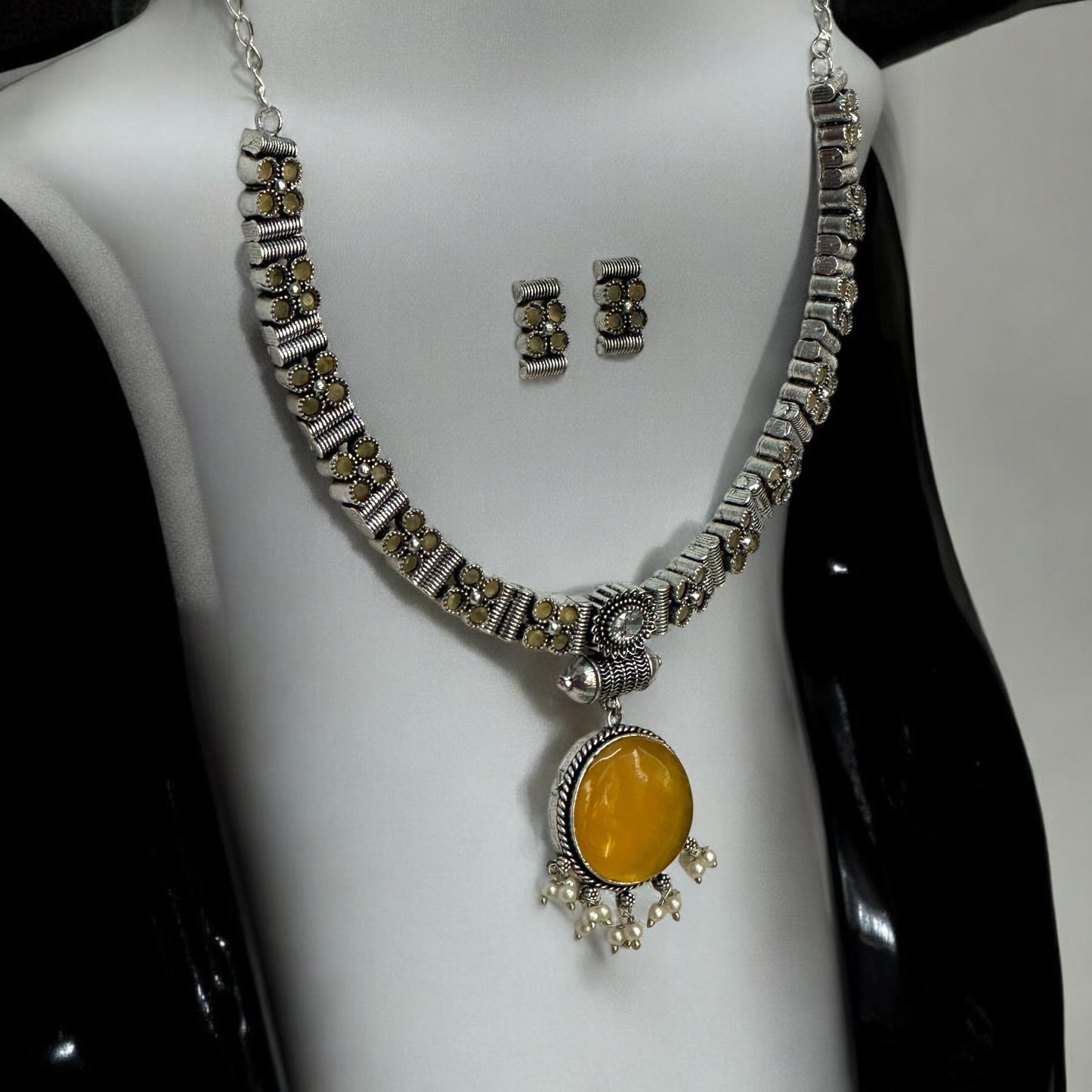 Side view of Silver look alike oxidised necklace set in yellow with circular pendant, pearl drops, and matching earrings displayed on white bust stand