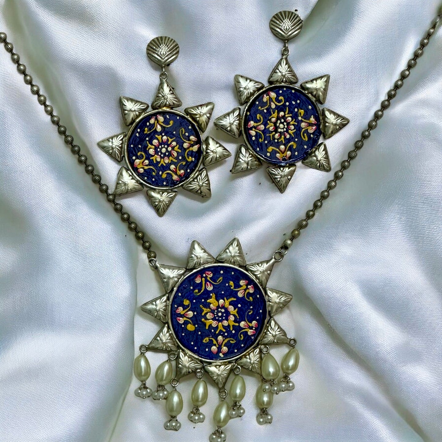 Oxidized silver replica necklace with large blue floral pendant and matching earrings on white fabric β Bella & Diva