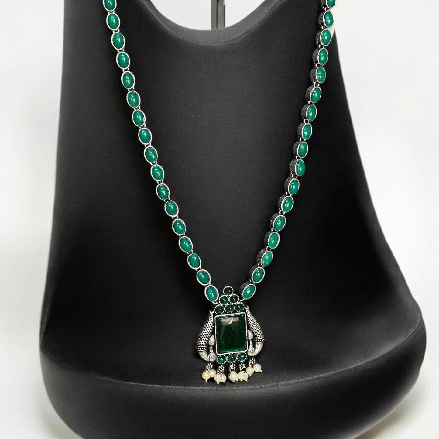 Silver look alike green stone necklace set displayed on a black stand – Indian designer jewellery by Bella & Diva.