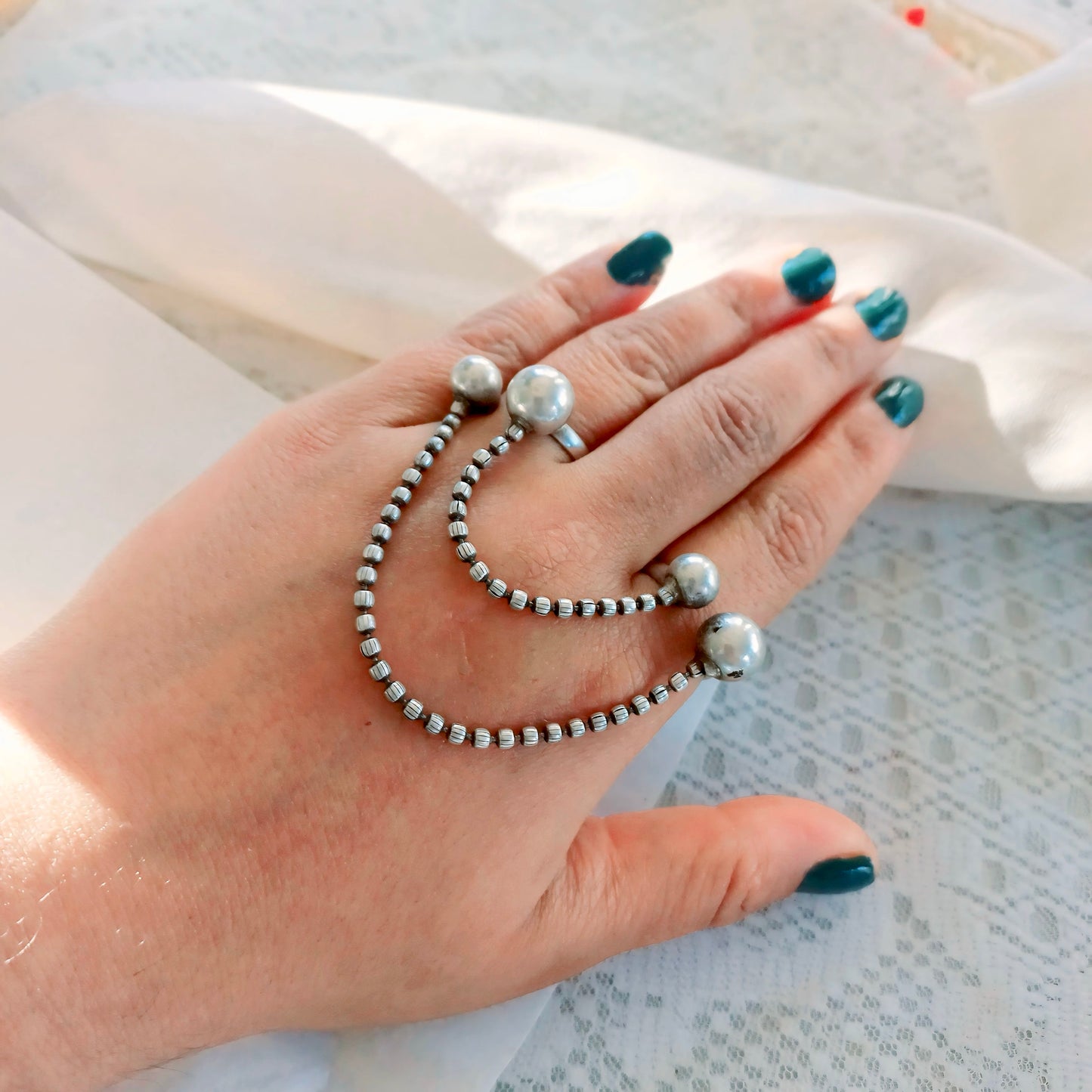A woman's hand adorned with a Silver Replica Adjustable Double Finger Ring, featuring silver-toned chain links and pearl-like accents draped across two fingers, creating a bold fashion statement.