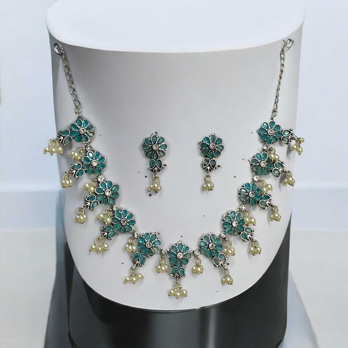 Silver Replica Necklace Set in Sky Blue featuring delicate floral motifs adorned with pearl accents, paired with matching earrings, displayed on a white and black mannequin stand.