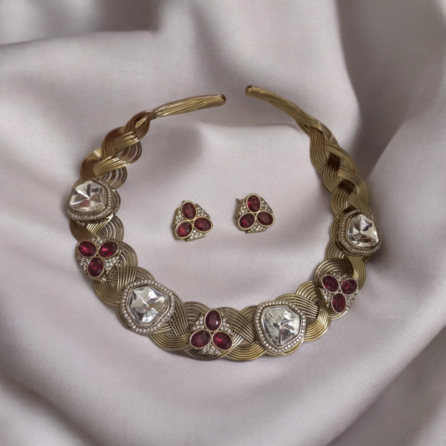 Statement hasli necklace with Apala polish in gold and ruby tones, featuring moissanite stones and matching earrings, laid against a an off white fabric.