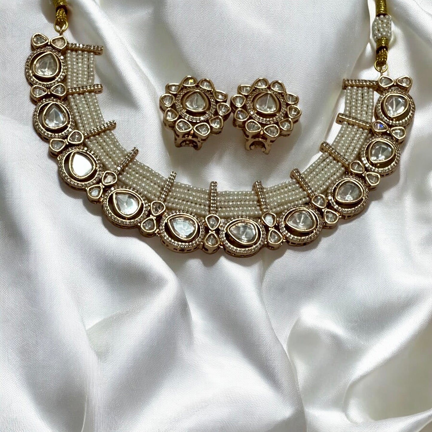 Tyani Kundan pearl necklace set with large matching studs displayed on shiny white silk fabric β Bella & Diva