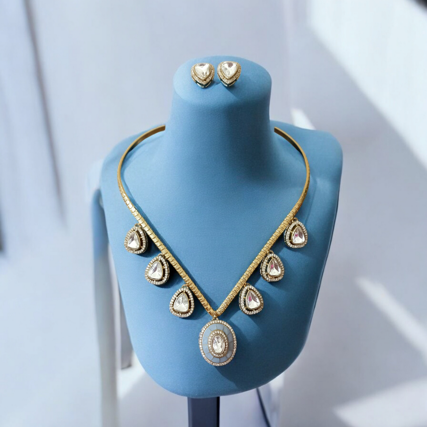 Handmade V-shaped Apala polish hasli necklace with moissanite stones and grey accents, paired with matching earrings, displayed on a blue stand.