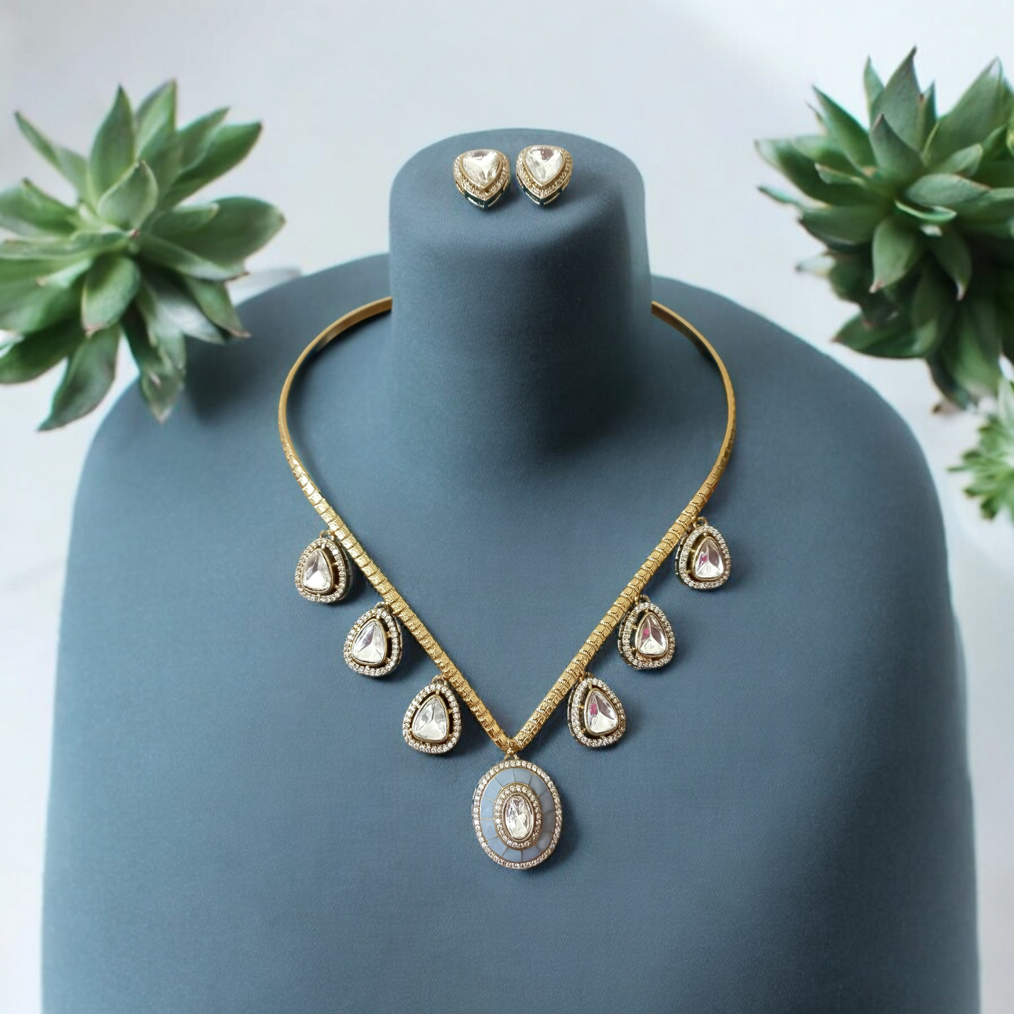 Handmade V-shaped Apala polish hasli necklace with moissanite stones and grey accents, paired with matching earrings, displayed on a greenish blue coloured jewellery display stand.