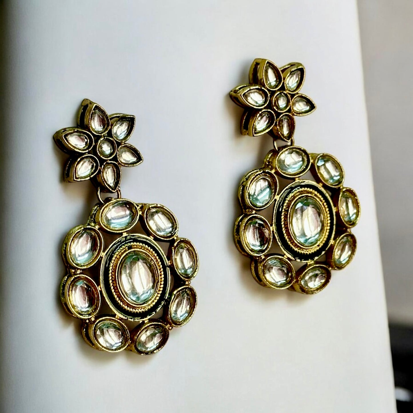 Elegant Kundan earrings featuring intricate floral designs in green and gold tones, placed on a white coloured jewellery display stand. These are perfect for traditional and festive occasions. Now available on bellandiva.com.