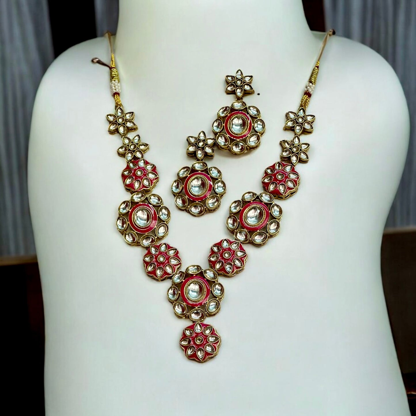 Elegant Kundan necklace set featuring intricate floral designs in pink and gold tones, paired with matching earrings, placed on a white coloured jewellery display stand. These are perfect for traditional and festive occasions.