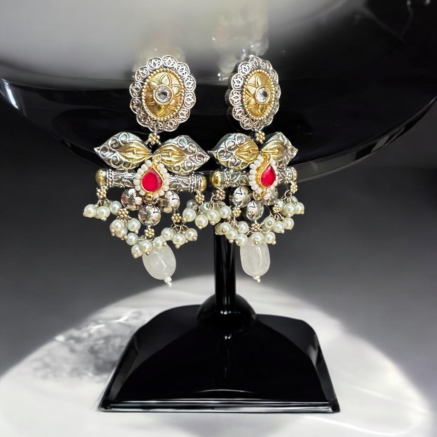 Amrapali dual-tone statement earrings featuring intricate pachi kundan and jadau work, adorned with vibrant pink stone and gold toned work with hanging pearls displayed on a black mannequin with a soft sunlight backdrop.