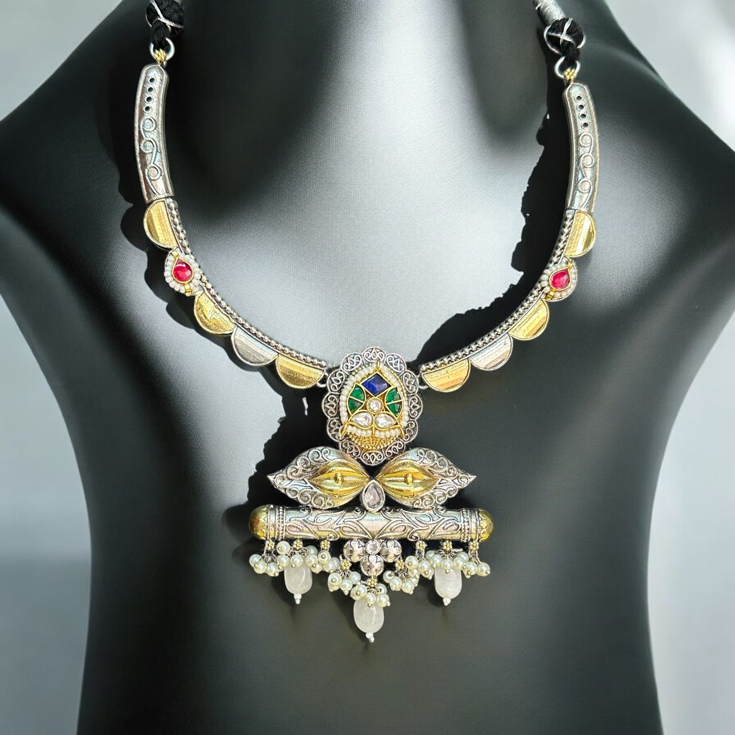Amrapali dual-tone hasli necklace  featuring intricate pachi kundan and jadau work, adorned with vibrant pink, green, and white stones, displayed on a black mannequin with a soft sunlight backdrop.