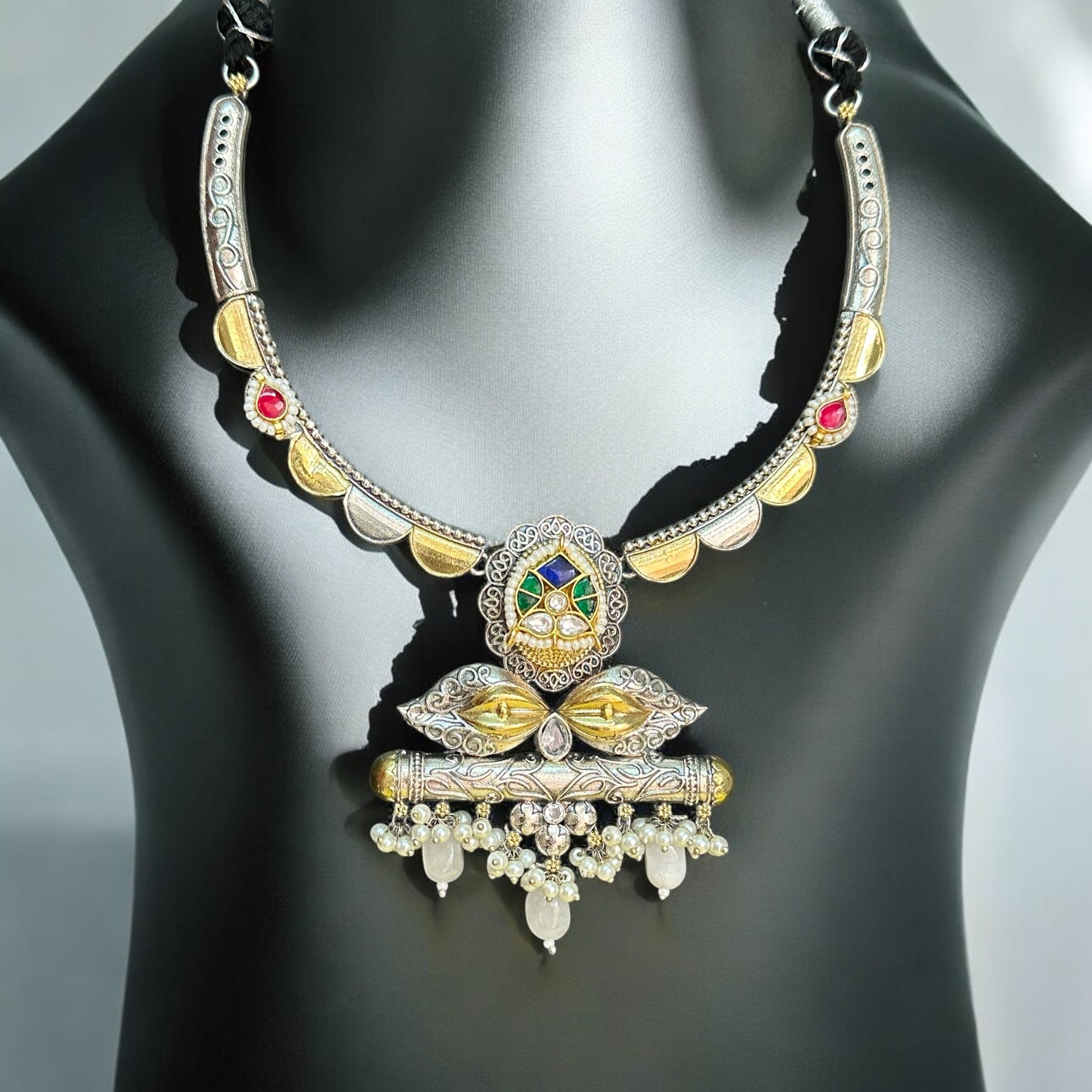 Amrapali dual-tone hasli necklace  featuring intricate pachi kundan and jadau work, adorned with vibrant pink, green, and white stones, displayed on a black mannequin with a soft sunlight backdrop.