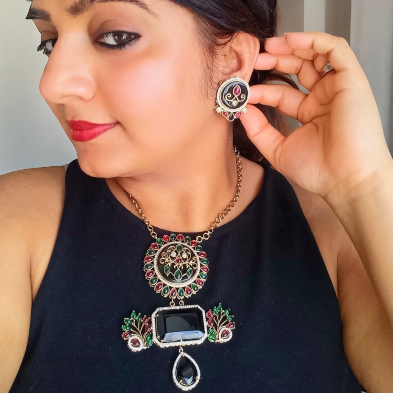 A model in black top displaying an Amrapali-style long necklace with intricate black, red, and green accents, paired with matching earrings in a fusion-inspired design to sell online in UK at bella and diva.