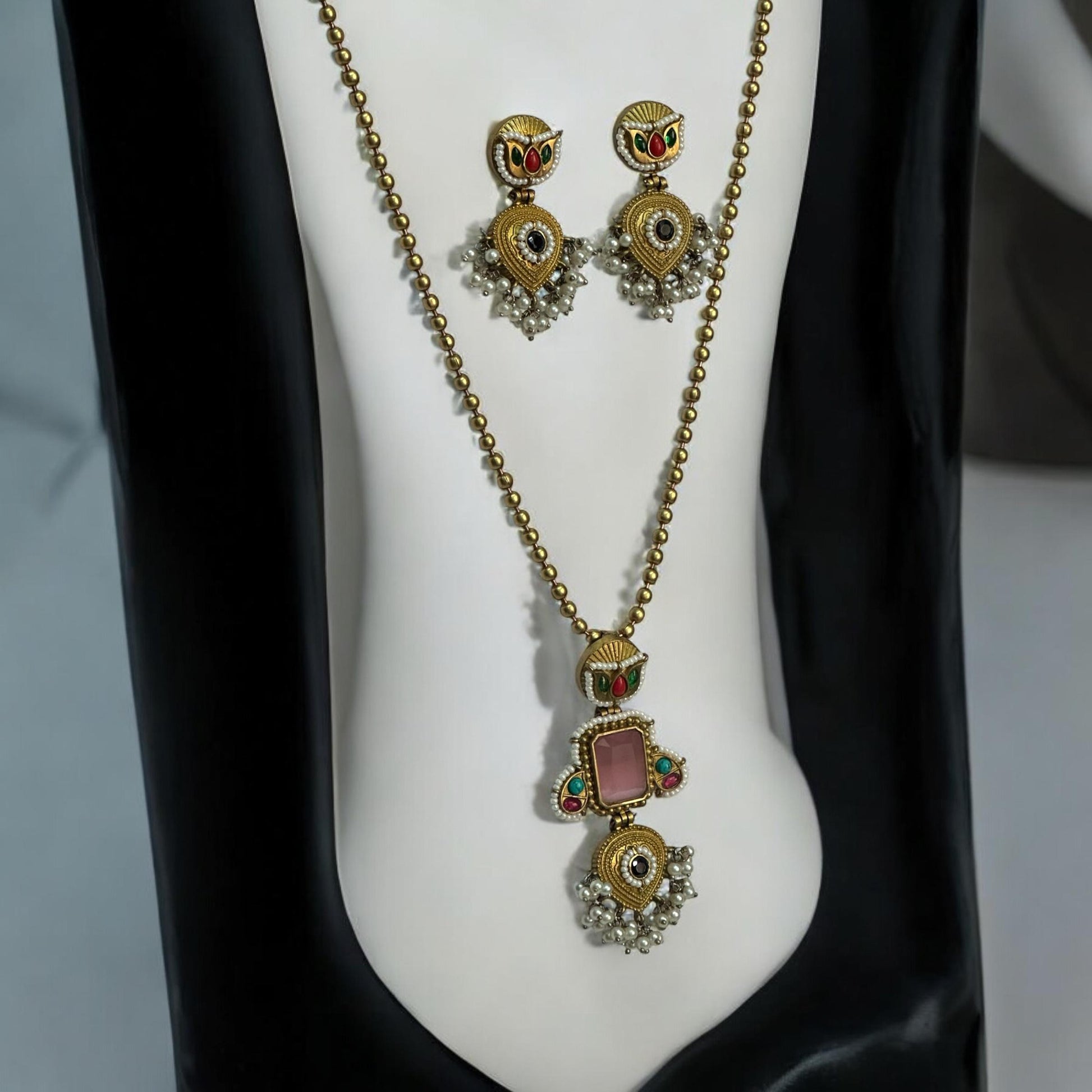 Amrapali Pachi Kundan Long Chain Pendant Set with Pink Monalisa Stone, featuring intricate detailing and matching earrings on a white and black jewellery display stand.