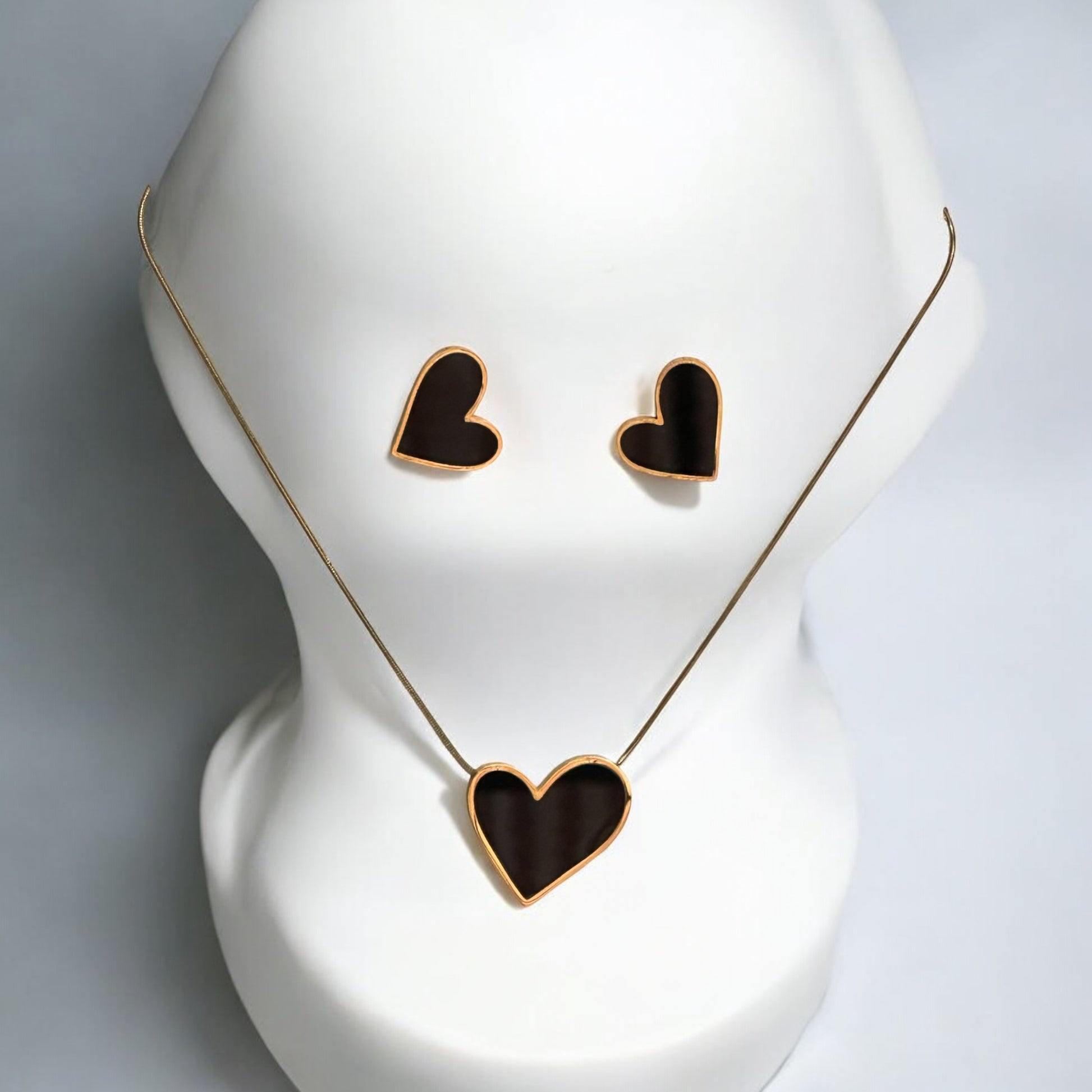 Anti-tarnish heart-shaped pendant set in gold finish with matching earrings placed on an off white jewellery display stand.