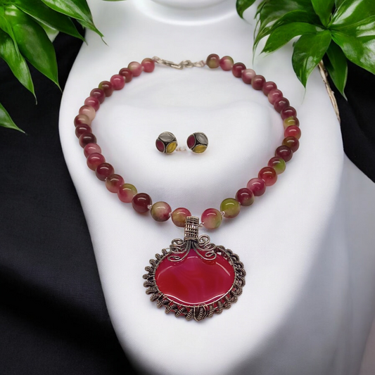 Beautiful Nature beads statement necklace with ear stud in dark pink colour placed on a white jewellery display stand with few green leaves to decorate the show. Best for casual and party wear.