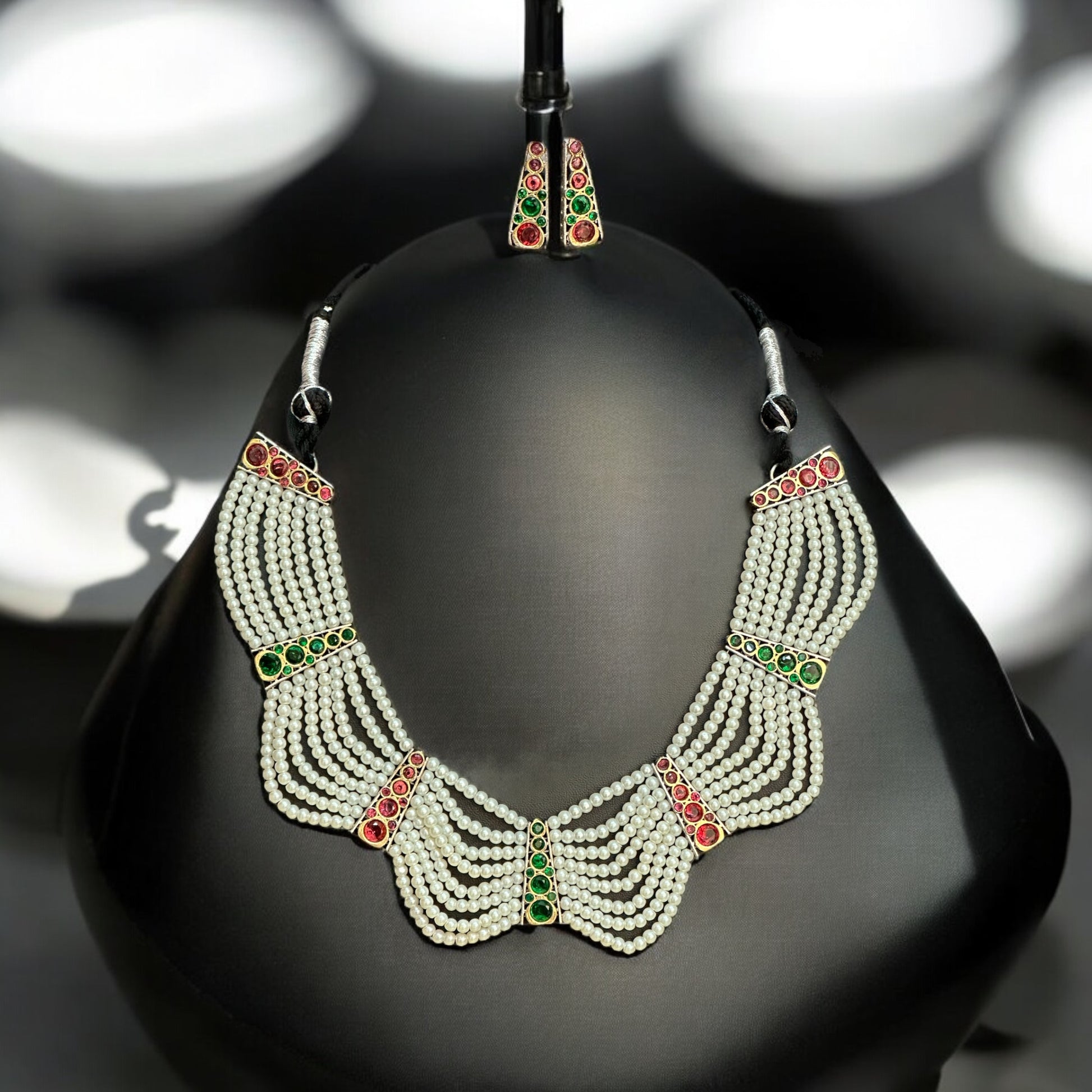 Elegant pearl necklace and earrings set with red and green stone accents, perfect for festive and traditional occasions placed on a black jewellery display stand.