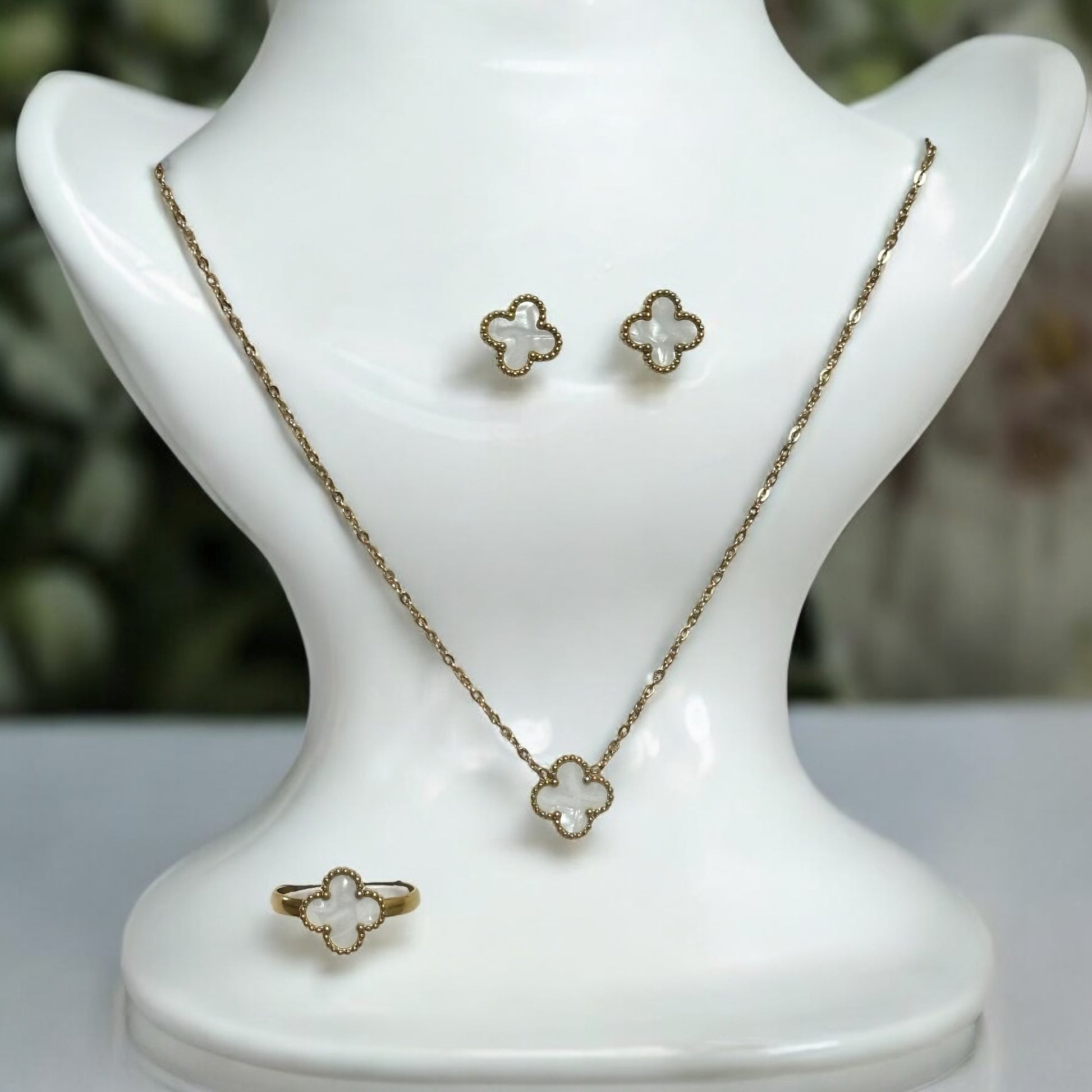 Elegant clover neck chain set featuring a delicate pendant, matching earrings, and a stylish finger ring in gold finish. It is displayed on a white coloured jewellery display stand.