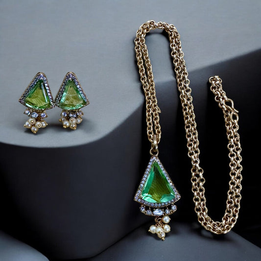 Green stoned Doublet American Diamond Pendant In Apala Polish With Earrings on a dark grey jewellery display stand.
