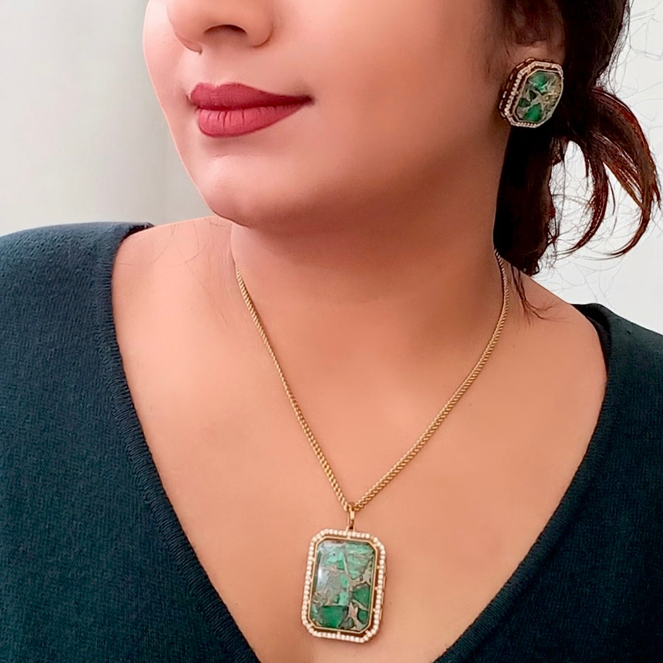 a model displaying Beautiful Doublet Green Diamond Chain Pendant Set with Earrings – gold-tone pendant set featuring a rectangular green doublet stone framed with shimmering diamonds. 