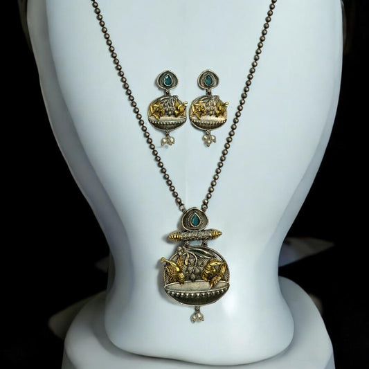 Front view of Dual tone German silver chain pendant set with gold floral and fish motifs, green stone accents, pearl drops, and matching earrings displayed on white jewellery stand