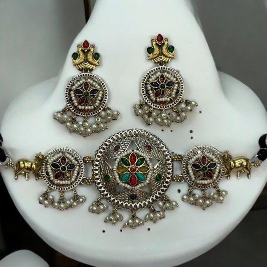 Dual tone German silver choker necklace set in multi colour with pearls, golden bull motifs, and matching earrings displayed on white jewellery stand