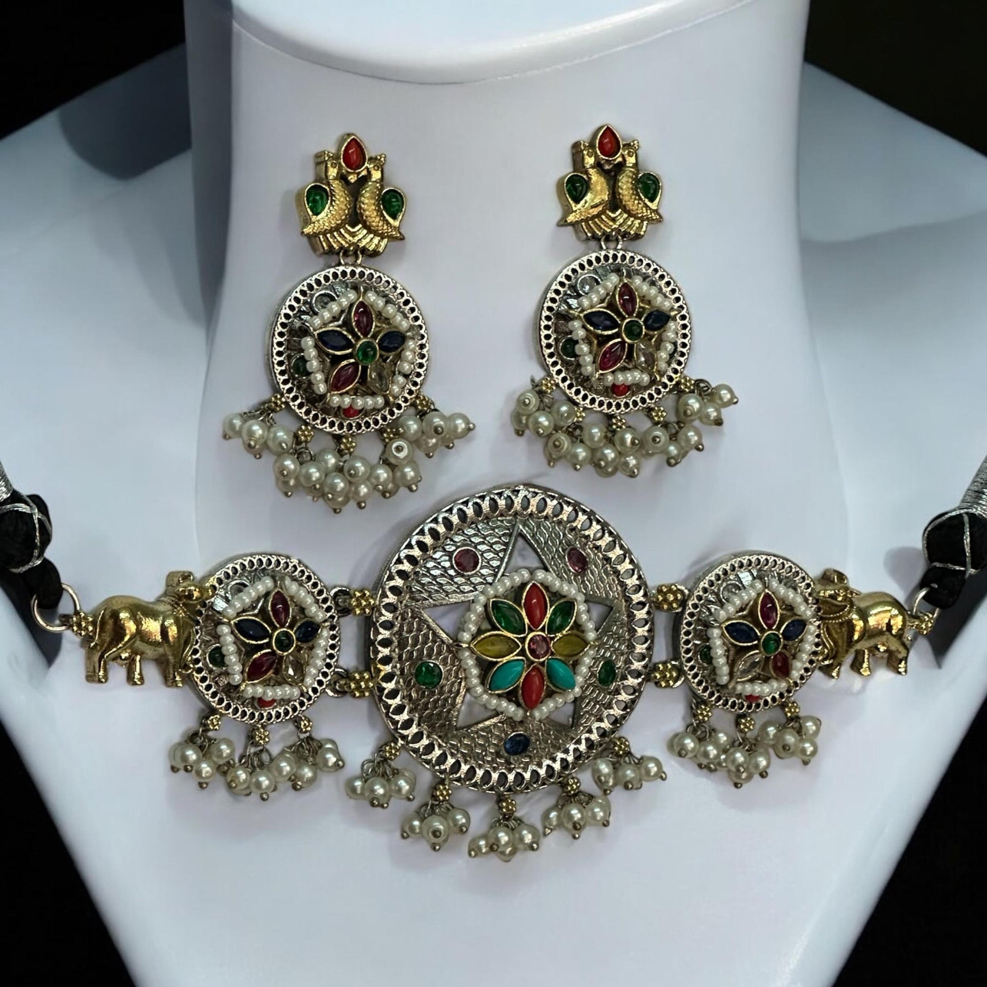 Side view of Dual tone German silver choker necklace set in multi colour with pearls, golden bull motifs, and matching earrings displayed on white jewellery stand