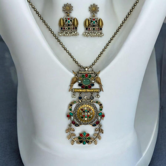 Dual Tone Apala Pachi Kundan Pendant Set with Navaratna Stones and Matching Earrings placed on a white coloured jewellery display stand.