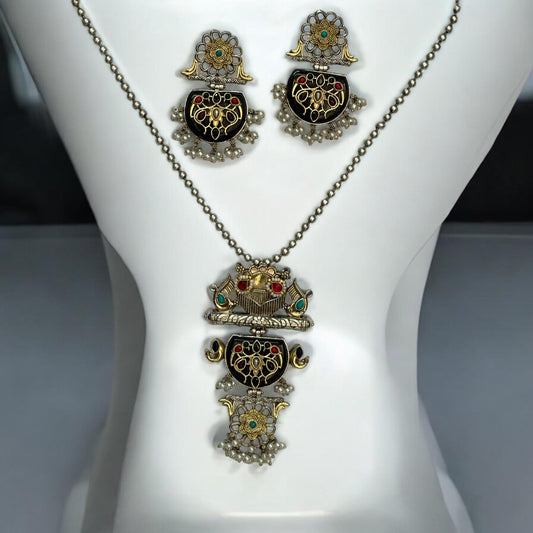 Dual Tone Apala Silver Long Pendant Set with Intricate Carving and Black Stone Finish, Featuring Matching Earrings placed on a white coloured jewellery display stand.