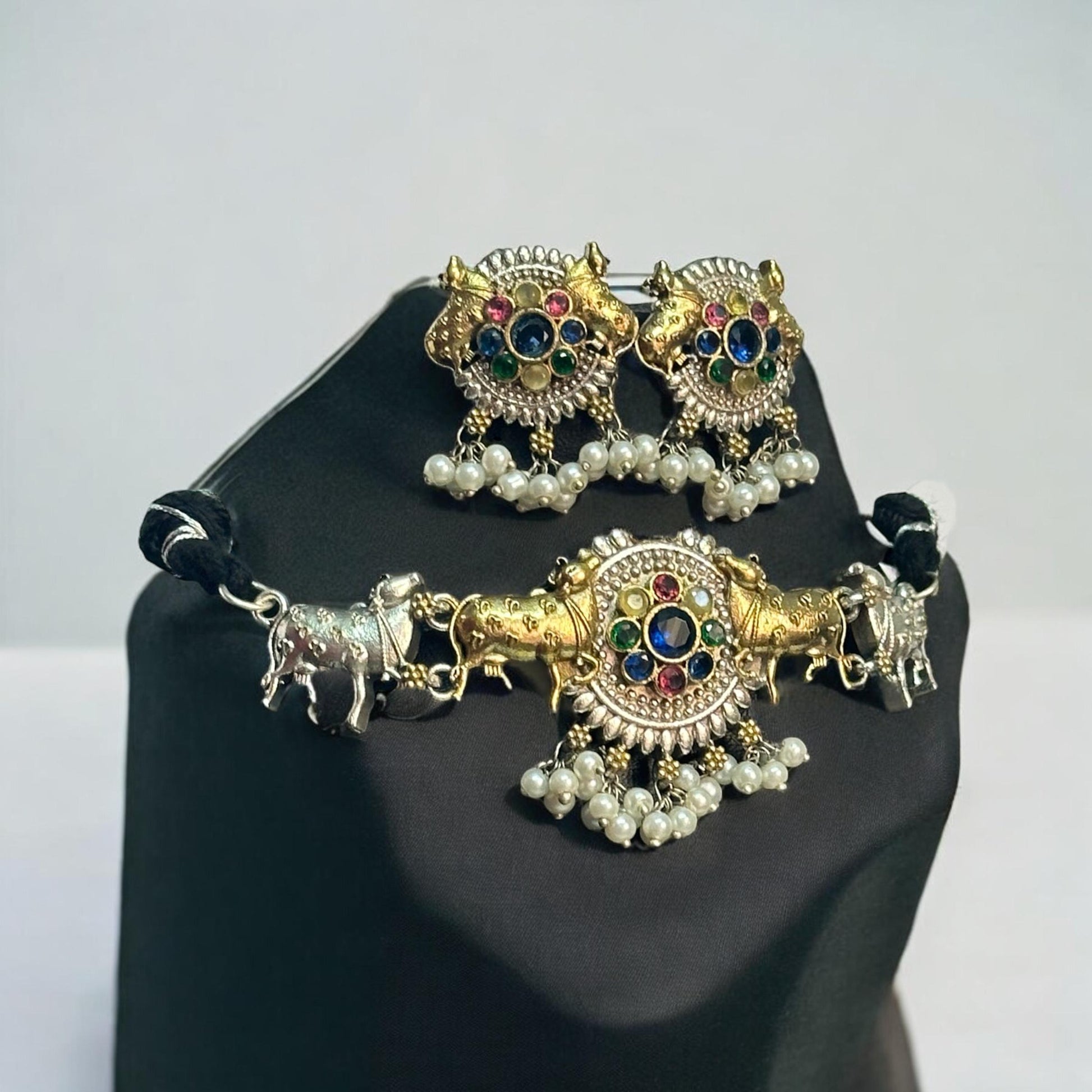 Dual Tone Silver Look-Alike Choker Set in Multi-Color with Intricate Nandi Design and Matching Earrings placed on a black coloured jewellery display stand. 