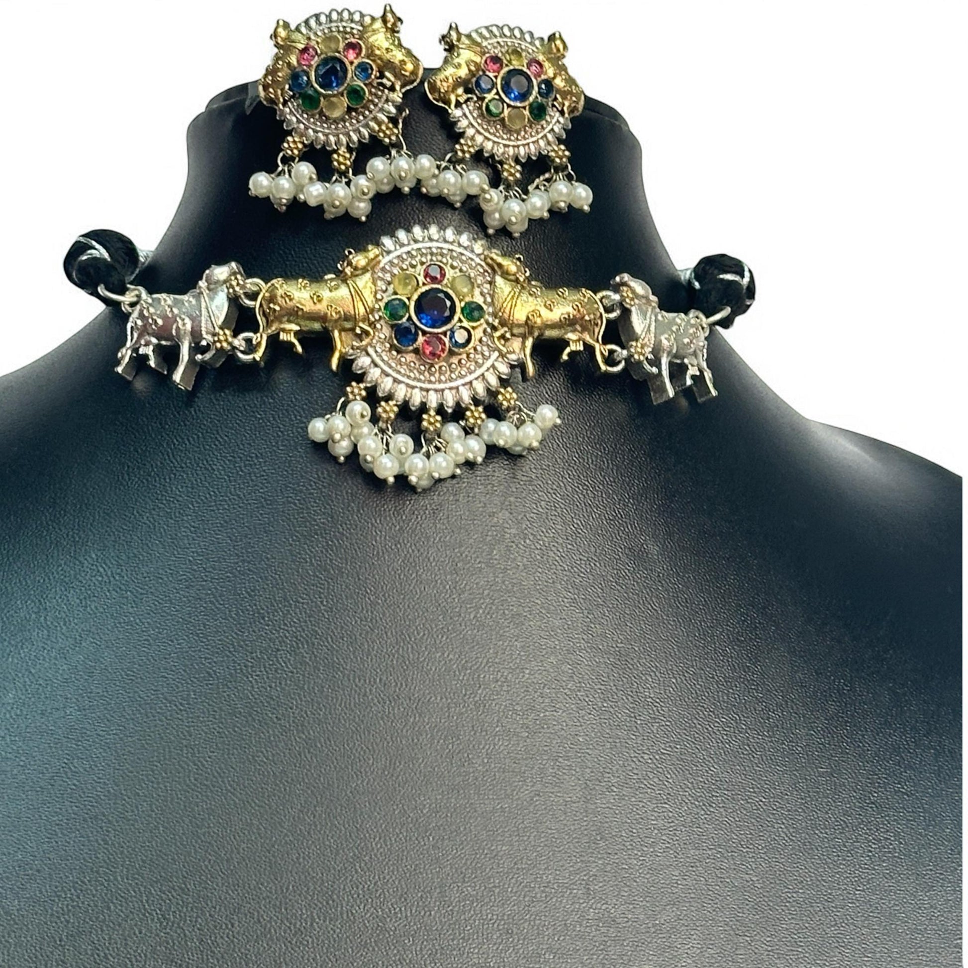 Dual Tone Silver Look-Alike Choker Set in Multi-Color with Intricate Nandi Design and Matching Earrings placed on a black coloured jewellery display stand. 